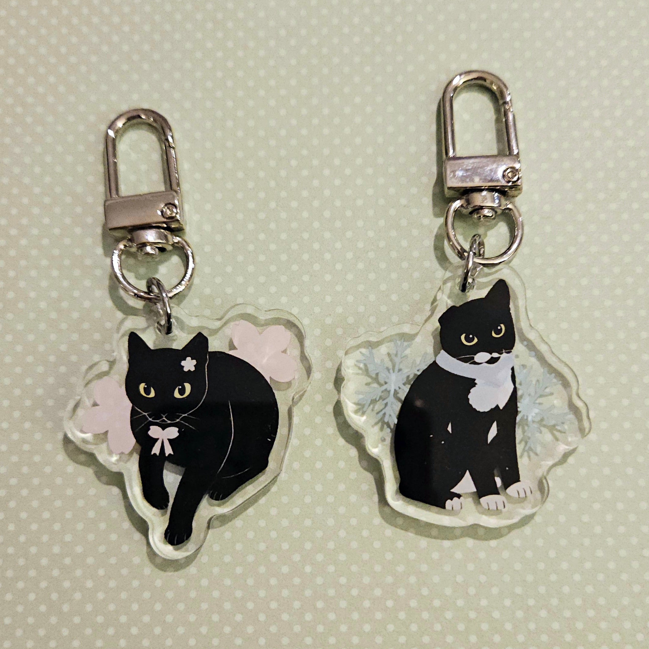 Two black cat keychains with white accents on a light green background