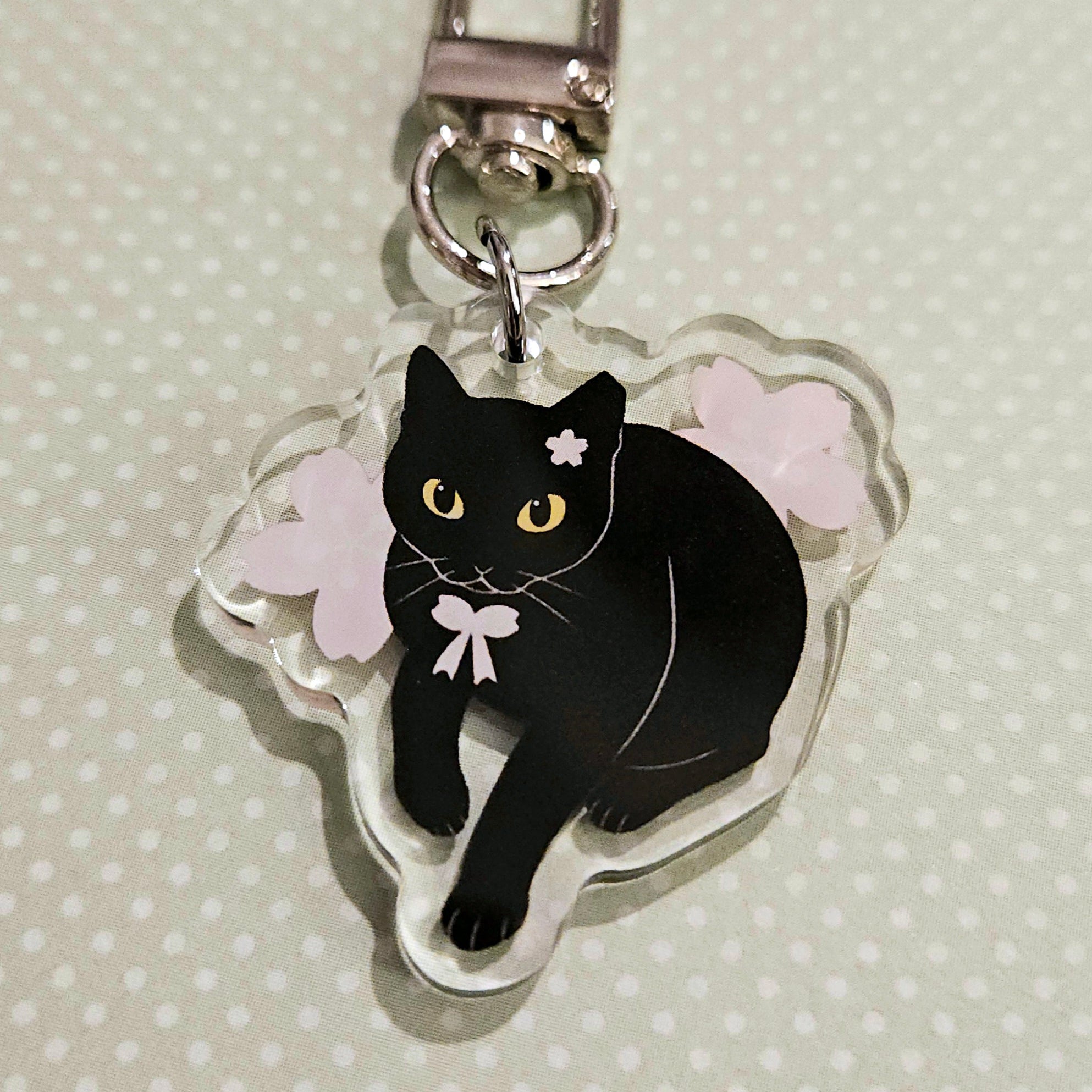 Black cat charm with a bow on a clear background with cherry blossoms