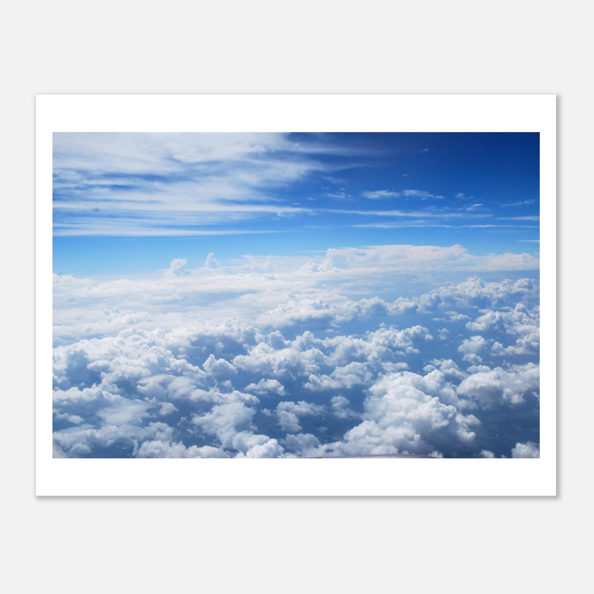 This is the 8" x 12" Above the Clouds Print by Lee Hansheng Studios. The rectangular stunning photograph of clouds captured from 36,000 feet above the earth, a breathtaking perspective that showcases the soft, ethereal beauty of the horizon. It is bright blue, dark blue, fluffs and streaks of clouds on the image. It has a white border and against a white background.