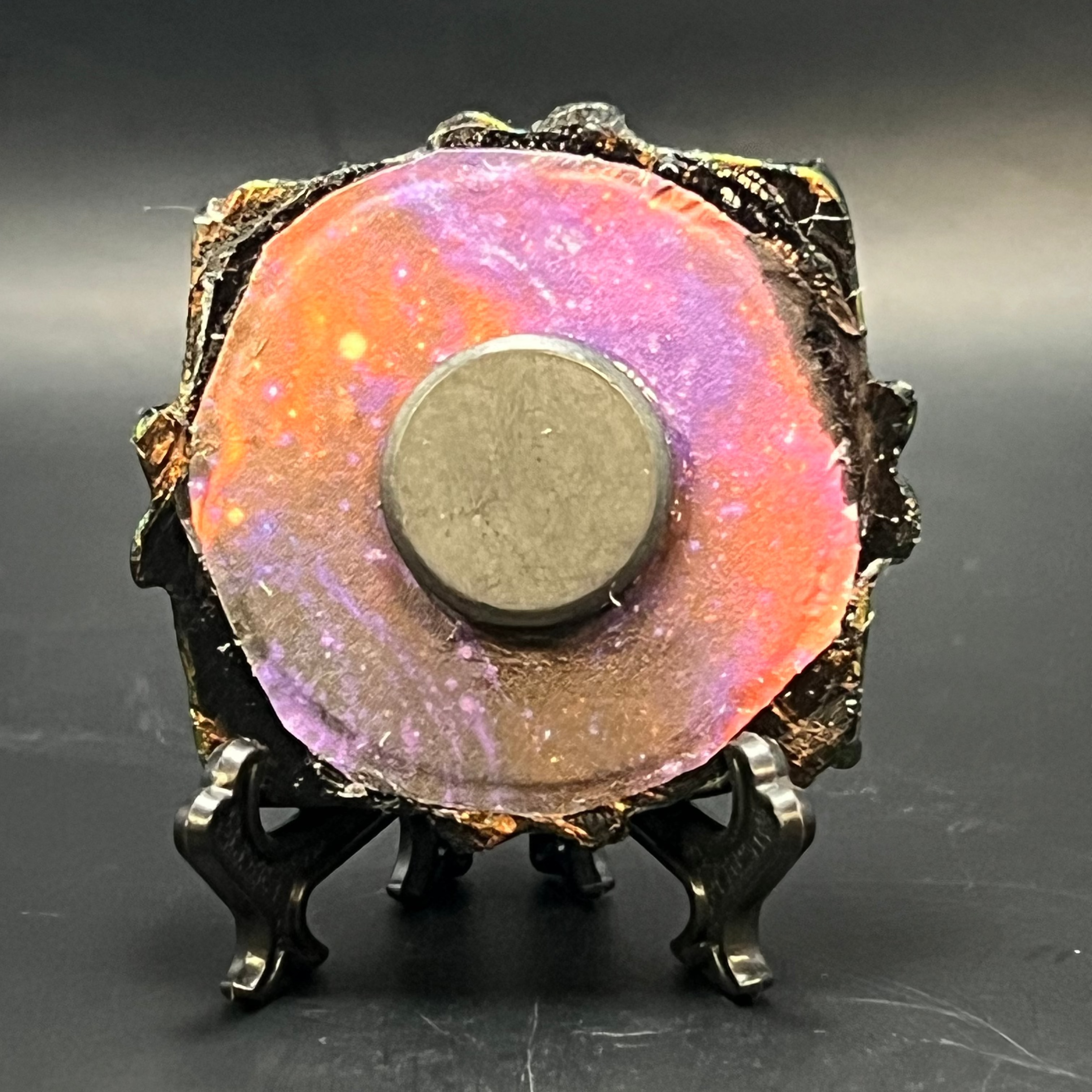 This is the handmade Ascension Miniature Painting by Chris Foster Design. This is showcasing the back. This is a small heart frame and the decorative item with a sparkly mix background with pink, orange and purple on a stand with yellow stars. There is a magnet and against a miniature picture frame.
