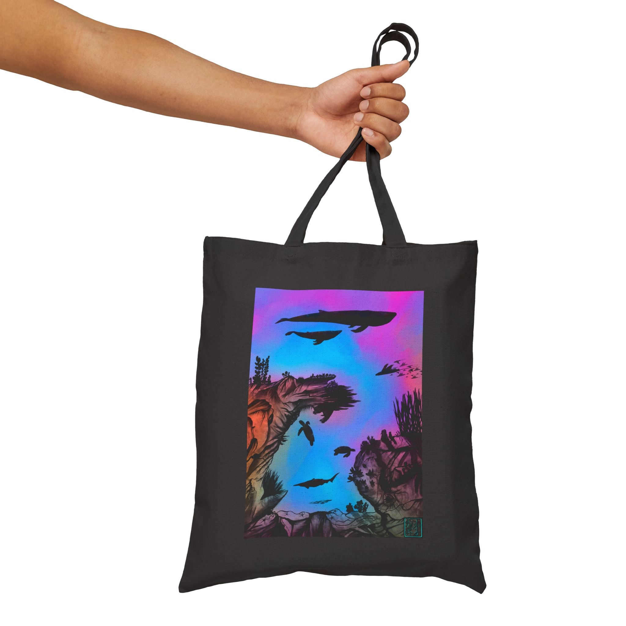 This is the Black Into the Abyss Canvas Tote by Lee Hansheng Studios.The illustration is underwater seascape with aquatic plants on a marbled background.There are two blue whales,1 goblin shark,school of eagle rays,two sea turtles and a school of fish.On the bottom right corner where the front patch of the backpack there is the studio logo printed in black outlined in blue.The colors are pink,purple,blue and red/orange.A man's upper arm is holding the handles from the left and against a white background.