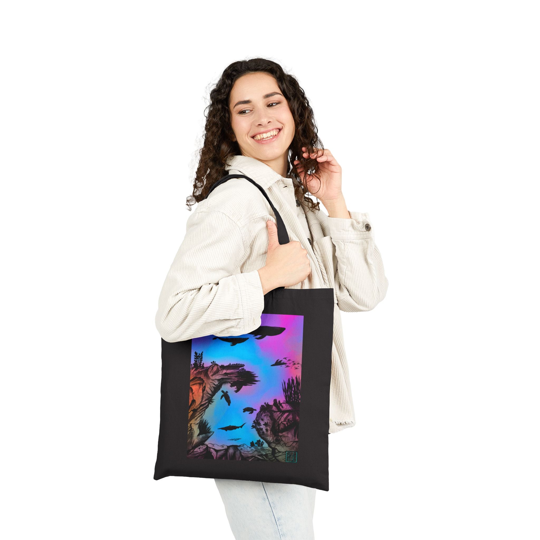 This is the Black Into the Abyss Canvas Tote by Lee Hansheng Studios.The illustration is underwater seascape with aquatic plants on a marbled background.There are two blue whales,1 goblin shark,school of eagle rays,two sea turtles and a school of fish.On the bottom right corner where the front patch of the backpack there is the studio logo printed in black outlined in blue.The colors are pink,purple,blue and red/orange.A woman is holding the tote on her arm with light colored clothes looking behind/smiling.