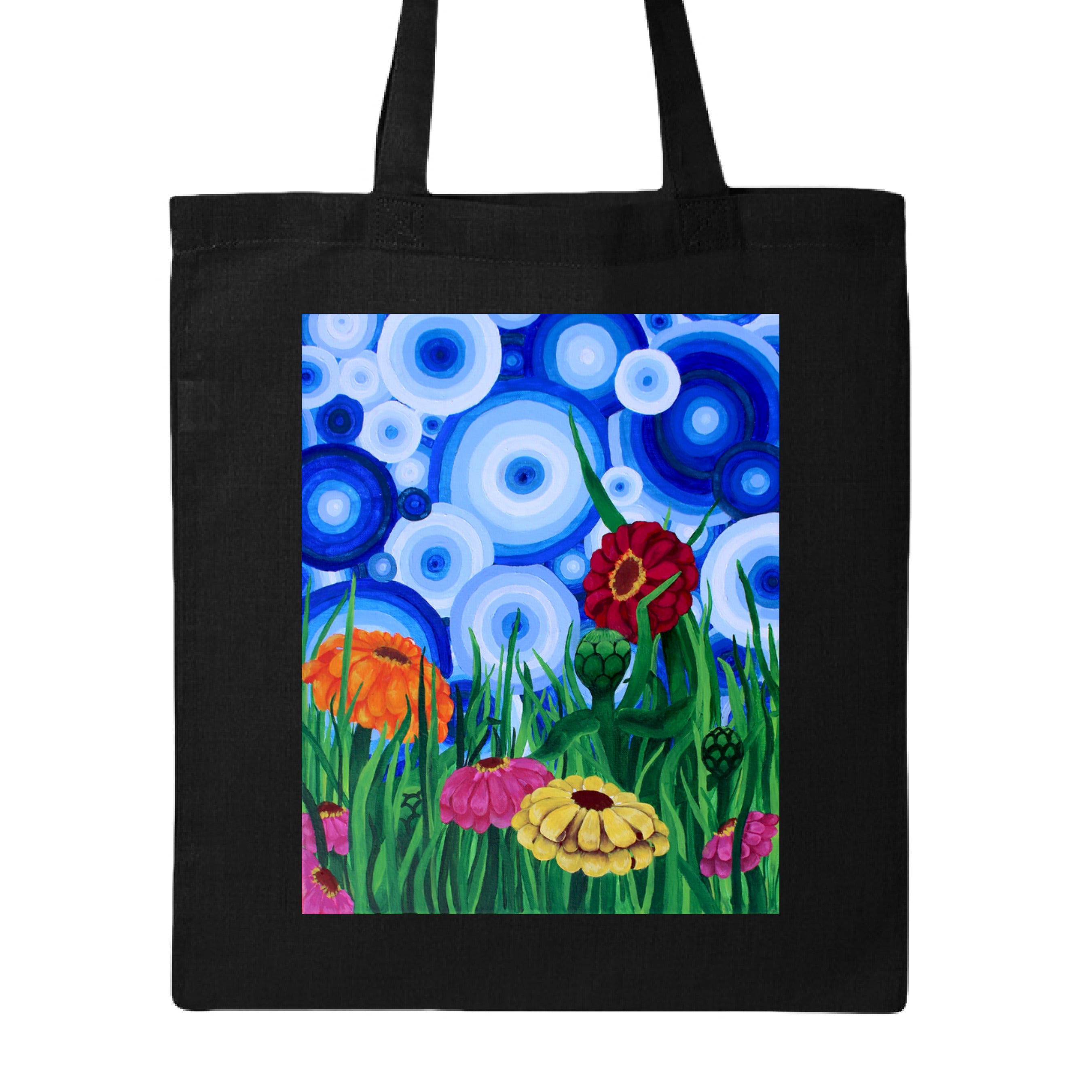 This is the Black Zinnia 2 Canvas Tote by Storm Garden Studio. This showcases the front of the tote. The rectangular illustration are bold and color zinnias like red, yellow and orange across tall green grass. The background has many different circles in blue, dark blue and white. The tote is against a white background.