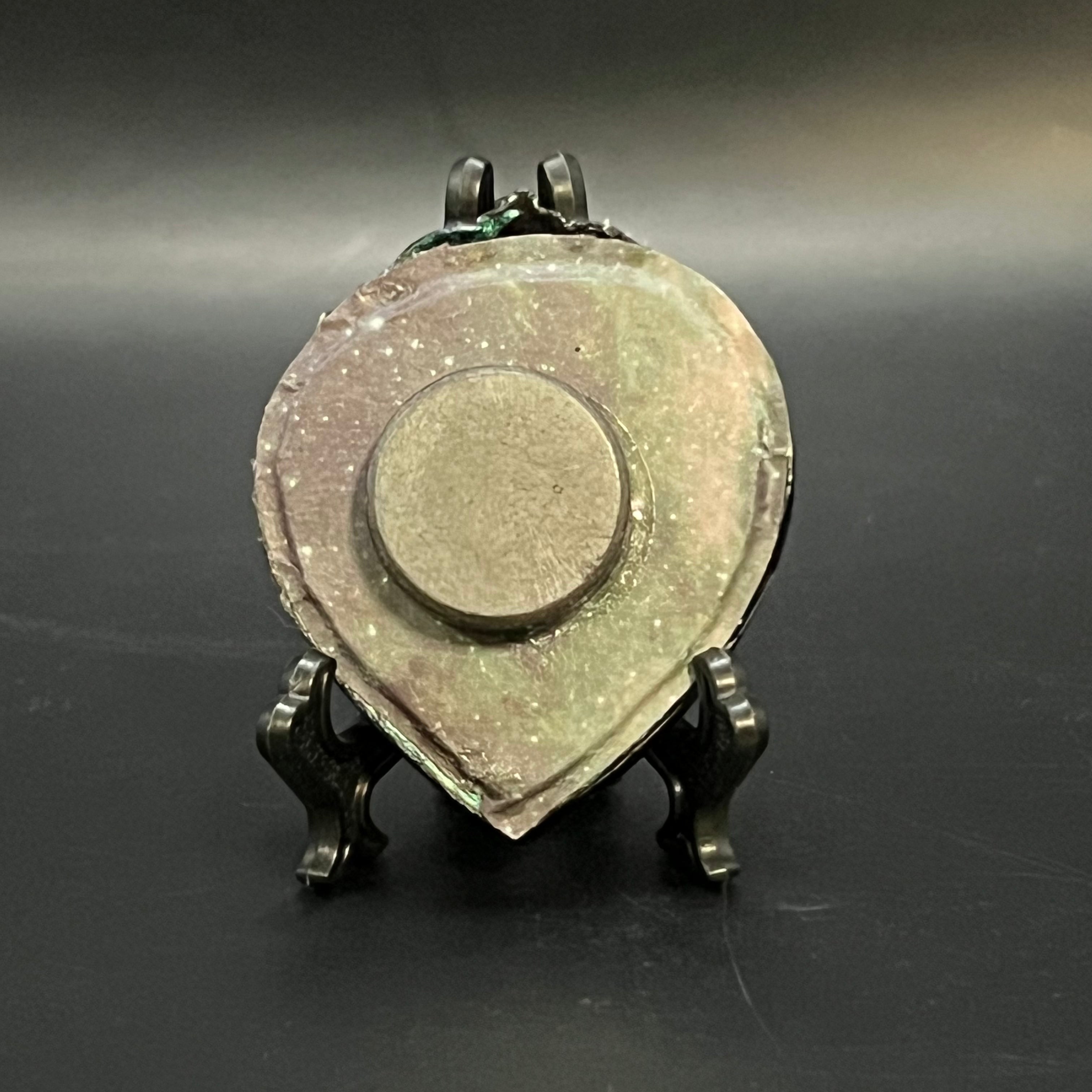 This is the Glowing Cluster Mini Painting by Chris Foster Design. This is showcasing the back. The backing is a dark galaxy with black, green and yellow stars. In the middle is a round magnet, on a black stand and against a dark background.