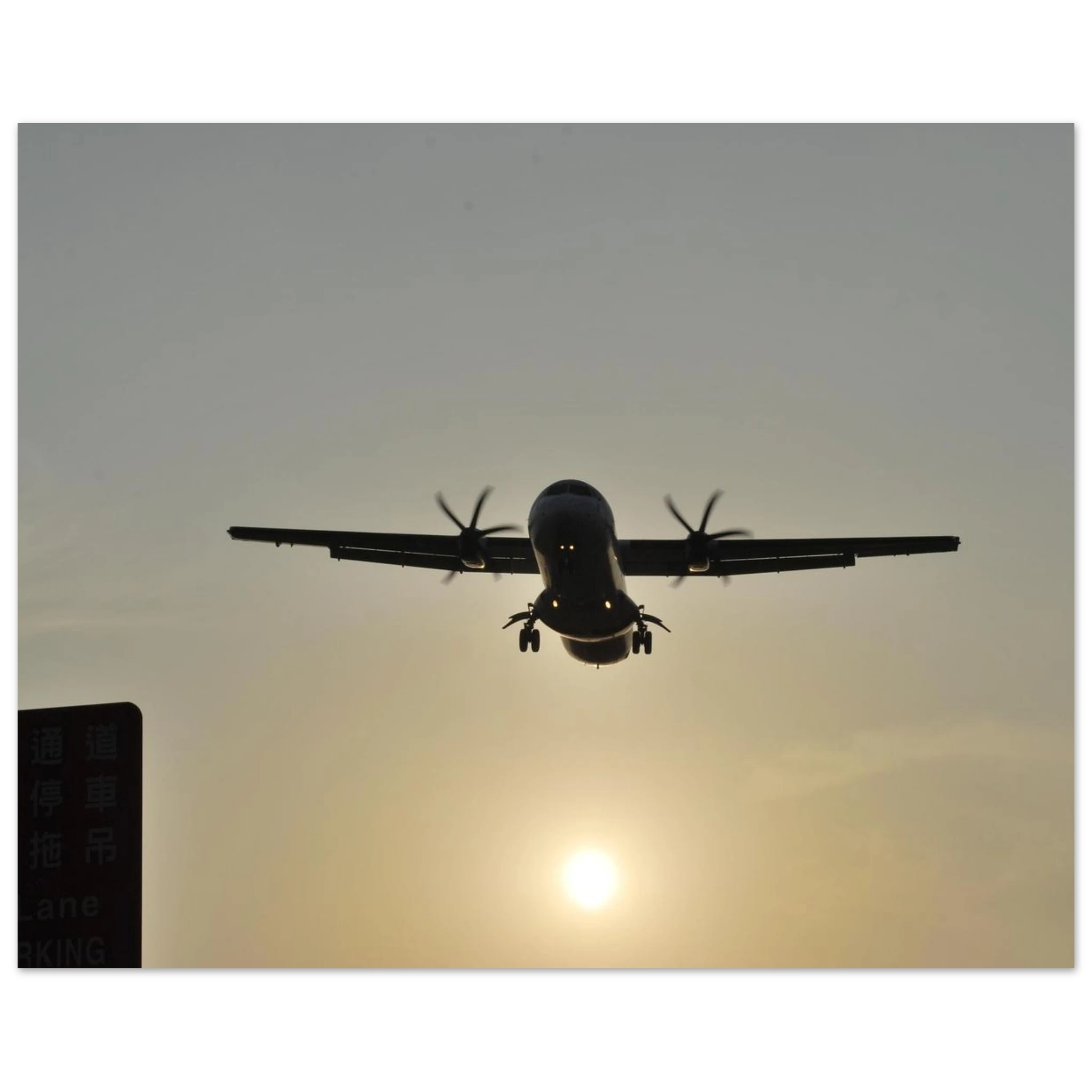 This is the 11" x 14" In Bound Print by Lee Hansheng Studios. It was captured at Songshan International Airport in Taipei, Taiwan, when the ATR 72 aircraft is taking flight. The airplane is flying against a sunset sky. On the left corner is a green sign in the shadows.