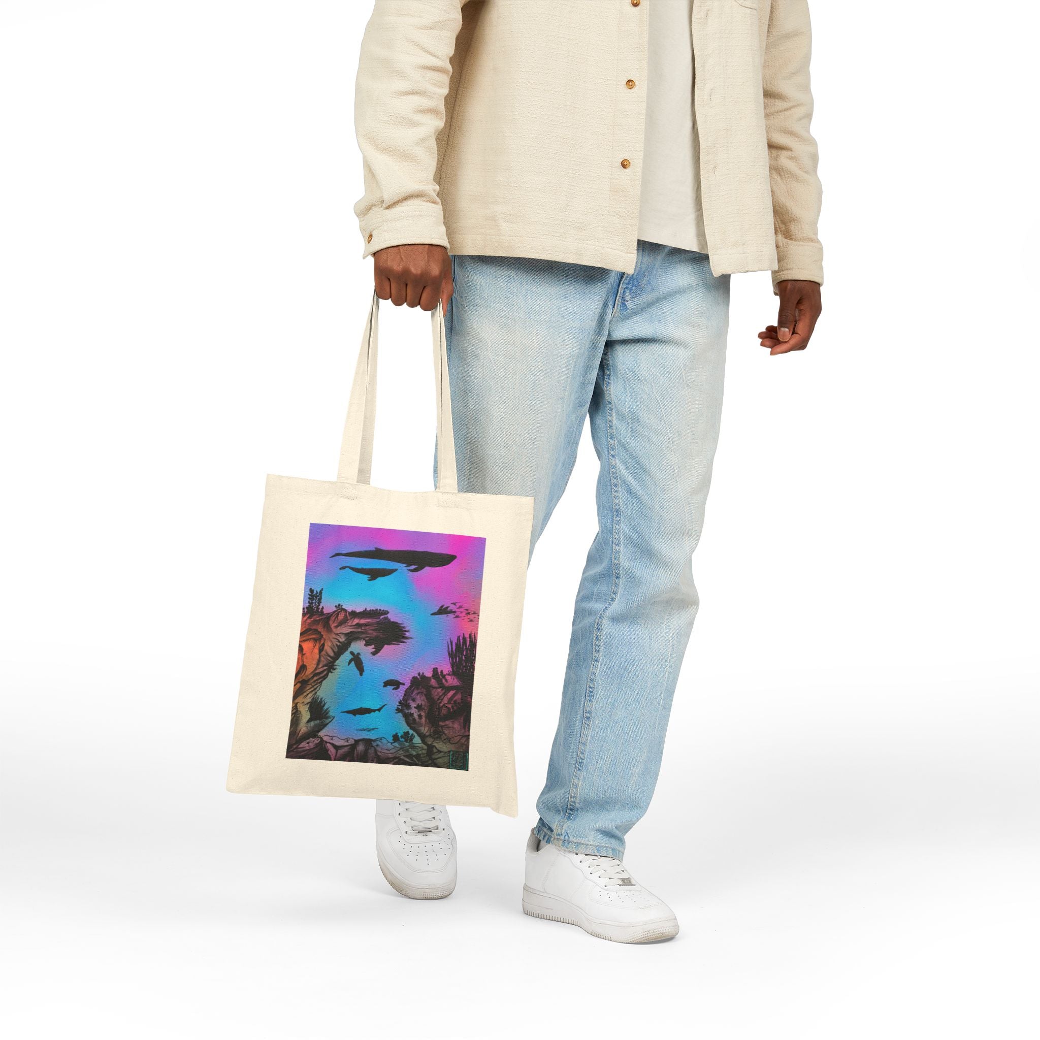 This is Natural Into the Abyss Canvas Tote by Lee Hansheng Studios.The illustration is underwater seascape with aquatic plants on a marbled background.There are two blue whales,1 goblin shark,school of eagle rays,two sea turtles and a school of fish.On the bottom right corner where the front patch of the backpack there is the studio logo printed in black outlined in blue.The colors are pink,purple,blue and red/orange.A guy is holding the tote in his left hand wearing white walking to the left.