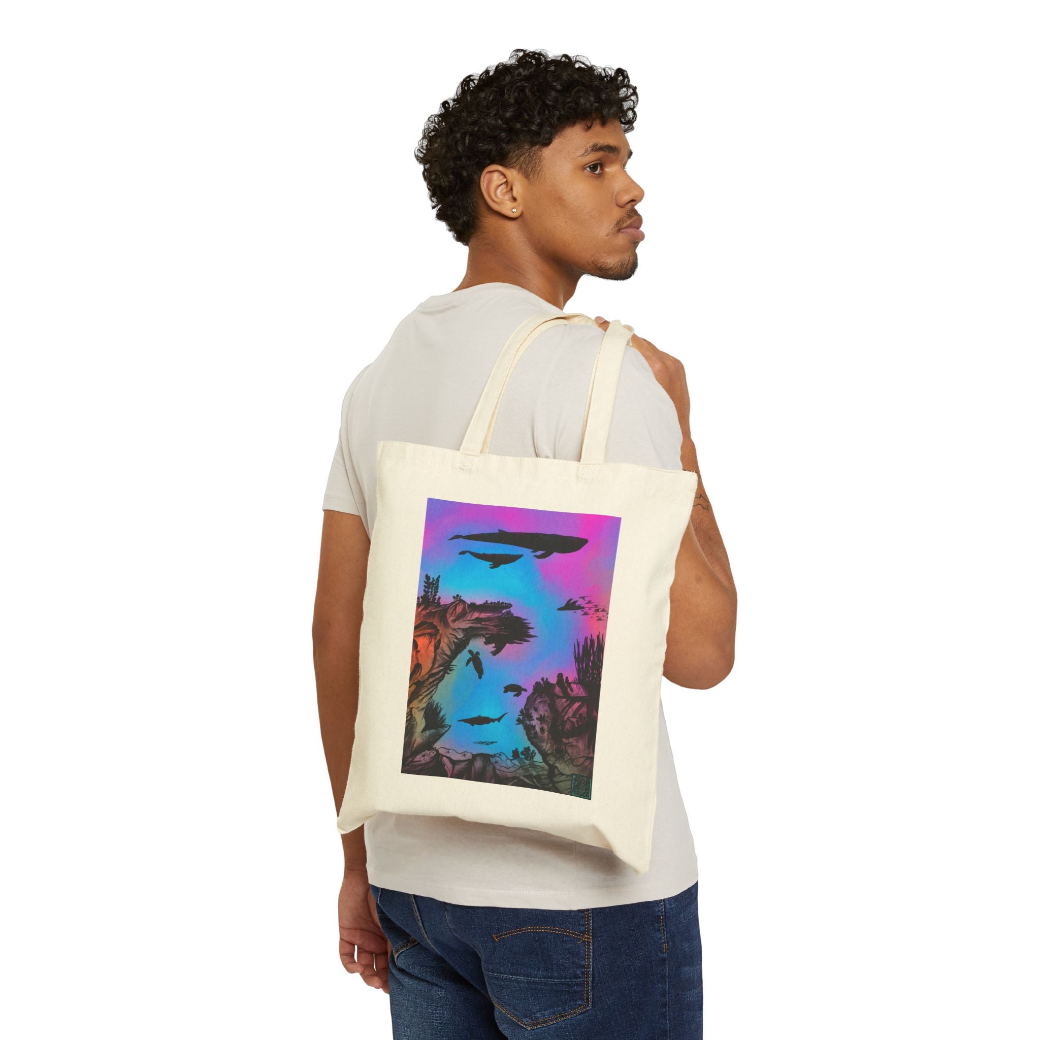 This is Natural Into the Abyss Canvas Tote by Lee Hansheng Studios.The illustration is underwater seascape with aquatic plants on a marbled background.There are two blue whales,1 goblin shark,school of eagle rays,two sea turtles and a school of fish.On the bottom right corner where the front patch of the backpack there is the studio logo printed in black outlined in blue.The colors are pink,purple,blue and red/orange.A man has the tote over his shoulder wearing jeans and white tee looking to the right.