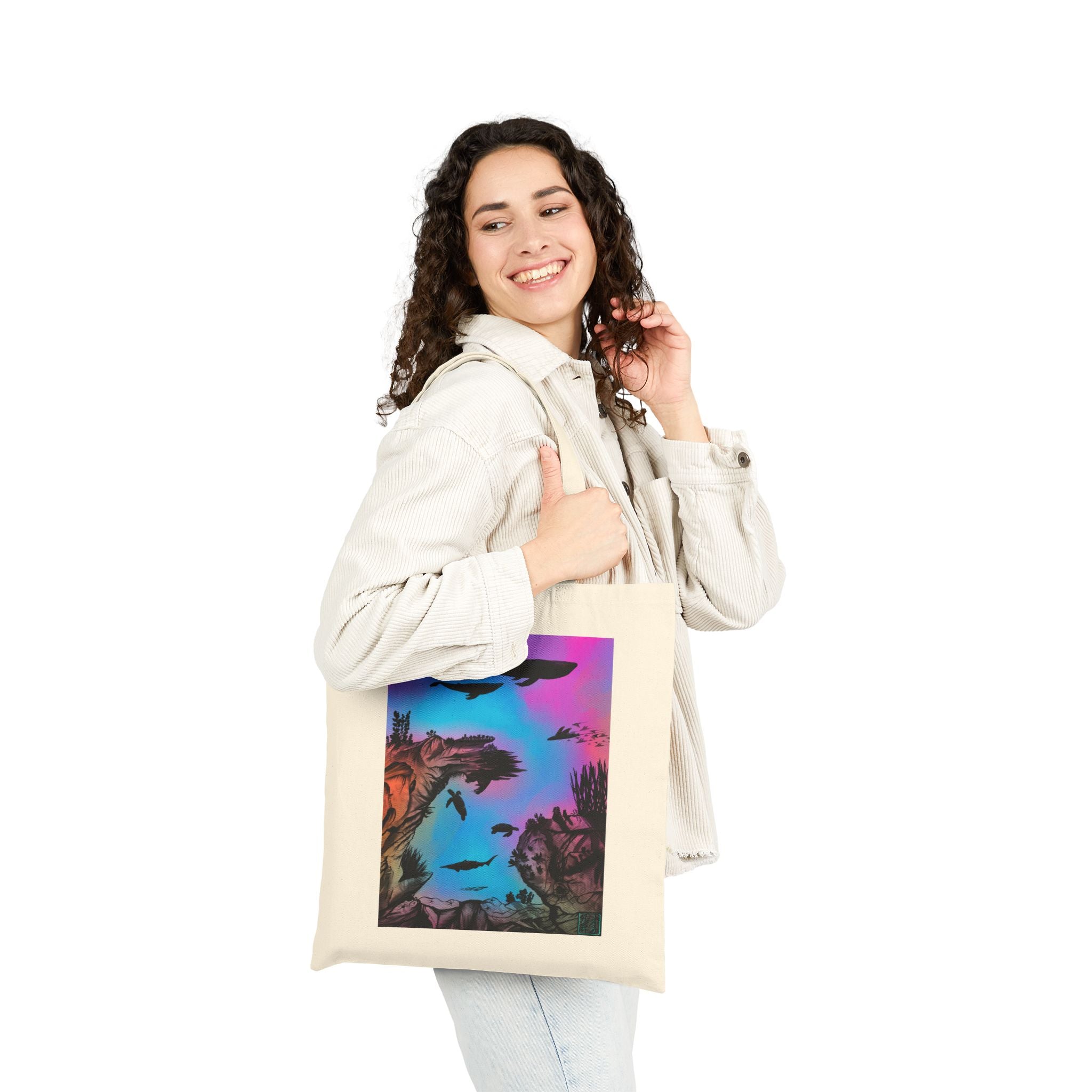This is Natural Into the Abyss Canvas Tote by Lee Hansheng Studios.The illustration is underwater seascape with aquatic plants on a marbled background.There are two blue whales,1 goblin shark,school of eagle rays,two sea turtles and a school of fish.On the bottom right corner where the front patch of the backpack there is the studio logo printed in black outlined in blue.The colors are pink,purple,blue and red/orange.A woman is holding the tote on her arm with light colored clothes looking behind/smiling.