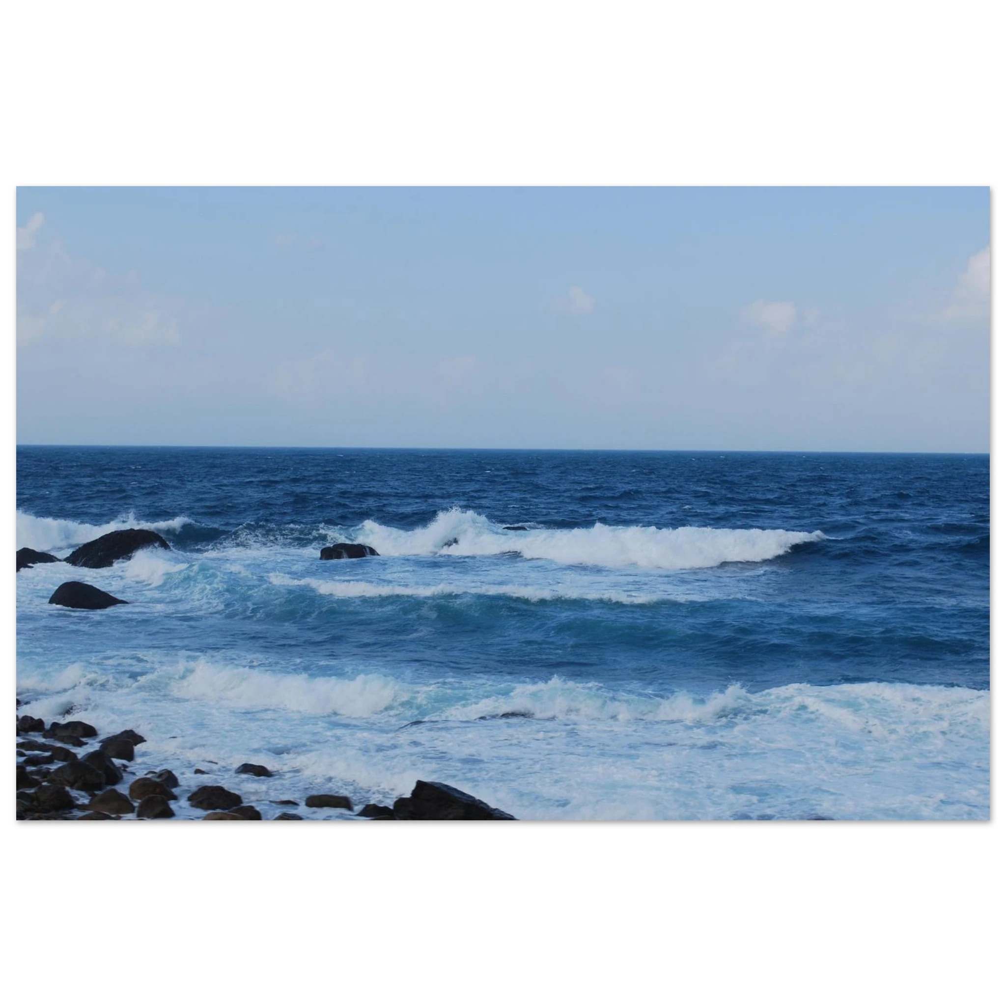 This is the 8" x 12" Rolling Print by Lee Hansheng Studios. This is a photgraph captured from Taiwan's nothern coastline. The waves crash against the rocky shore. The colors range from deep blues and frothy whites as the water comes in. The sky is cloudy with hints of white clouds but the rest is a lighter blue.