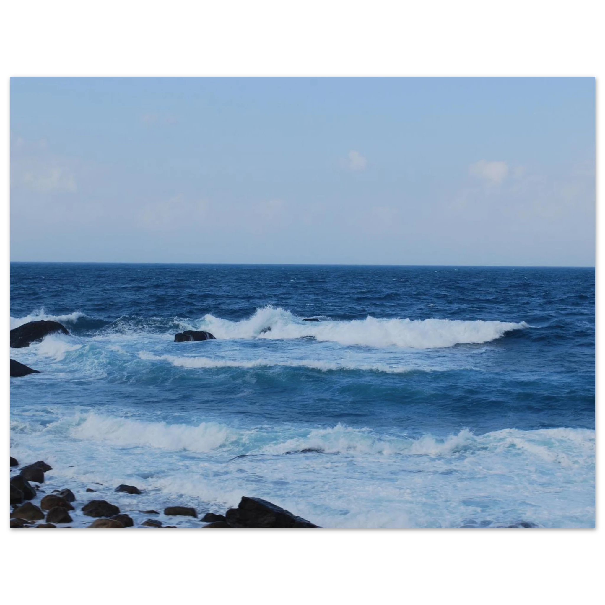 This is the 11" x 17" Rolling Print by Lee Hansheng Studios. This is a photgraph captured from Taiwan's nothern coastline. The waves crash against the rocky shore. The colors range from deep blues and frothy whites as the water comes in. The sky is cloudy with hints of white clouds but the rest is a lighter blue.