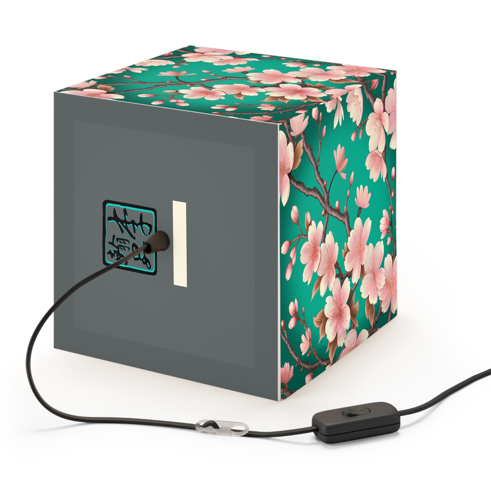 This is the Standard Sakura Light Cube Lamp by Lee Hansheng Studios. The illustration is all around has a blue/teal background, 3-4 thin dark wood branches with pink/light pink buds on each stem. There are blooming and already flowered sakuras on each branch. There is about 3-4 inches between the end of the illustration and the sides of the lamp. This includes plug for US or EU. The cube lamp is on a gray back where the logo and cord is plugged in. It is against a white background.