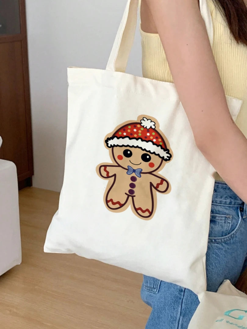 This is the White Ginger Bread, Ginger Dead Canvas Tote by Dazzle & Daggers Design. This is showcasing the front of the tote over a woman's shoulder wearing a yellow tank and light blue jeans, behind her is light wood, white sofa and a wood closet door. The illustration is of a tan ginger bread who is smiling, red circular cheeks, red zigzags on arm and legs. The gingerbread man is wearing a polka dotted hat with a white puff and lining around the hat.The polka dots are green, blue, purple white and orange.