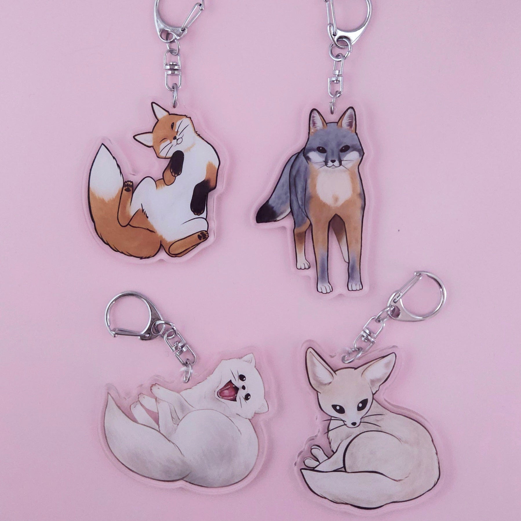 Four fox-themed keychains on a pink background