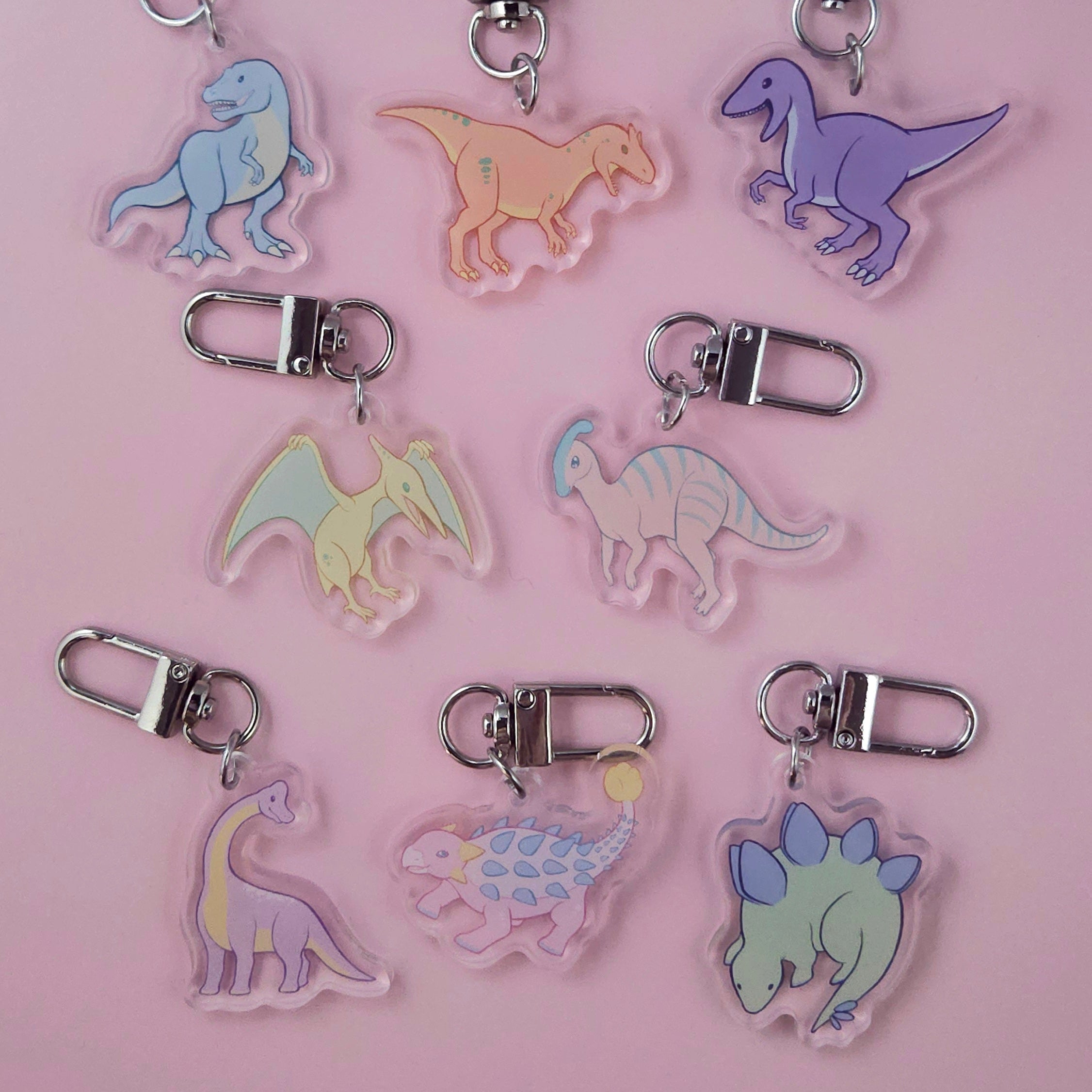 Set of dinosaur-shaped keychains on a pink background