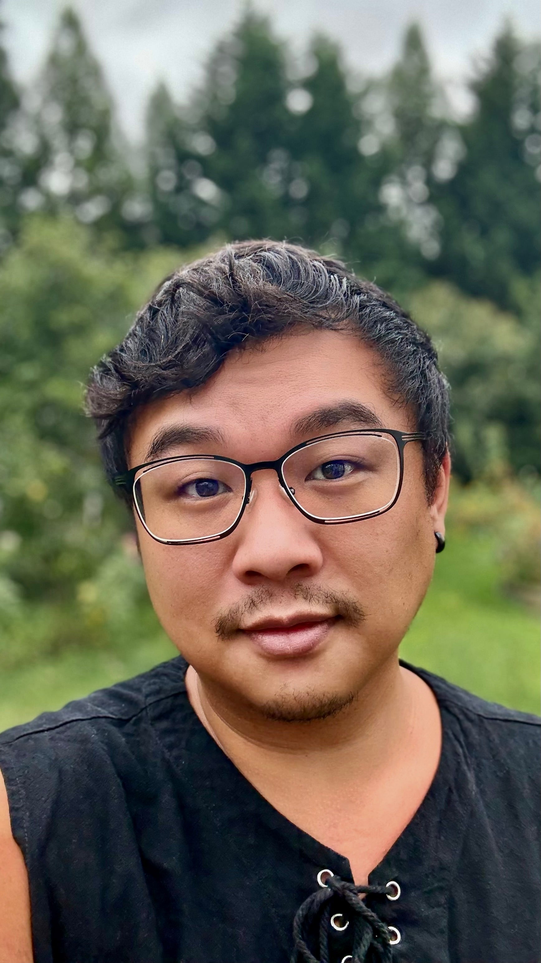 Hansheng Lee, outside in the garden wearing a black lace up tank and floating lens glasses