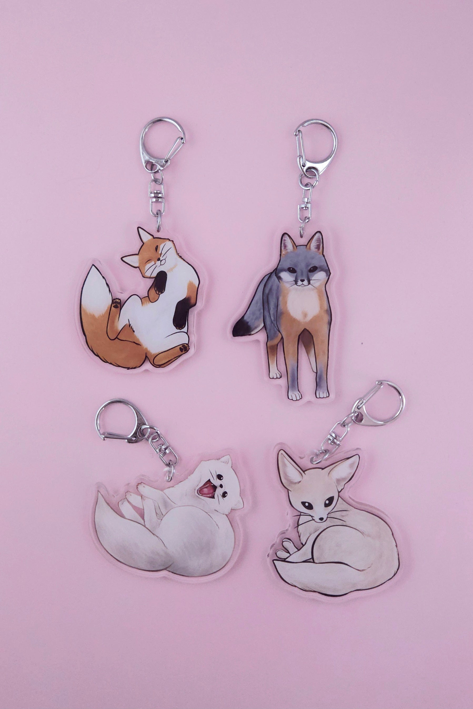 4 fox charms on steel keychains, fennec, grey, red, and arctic foxes on pink background