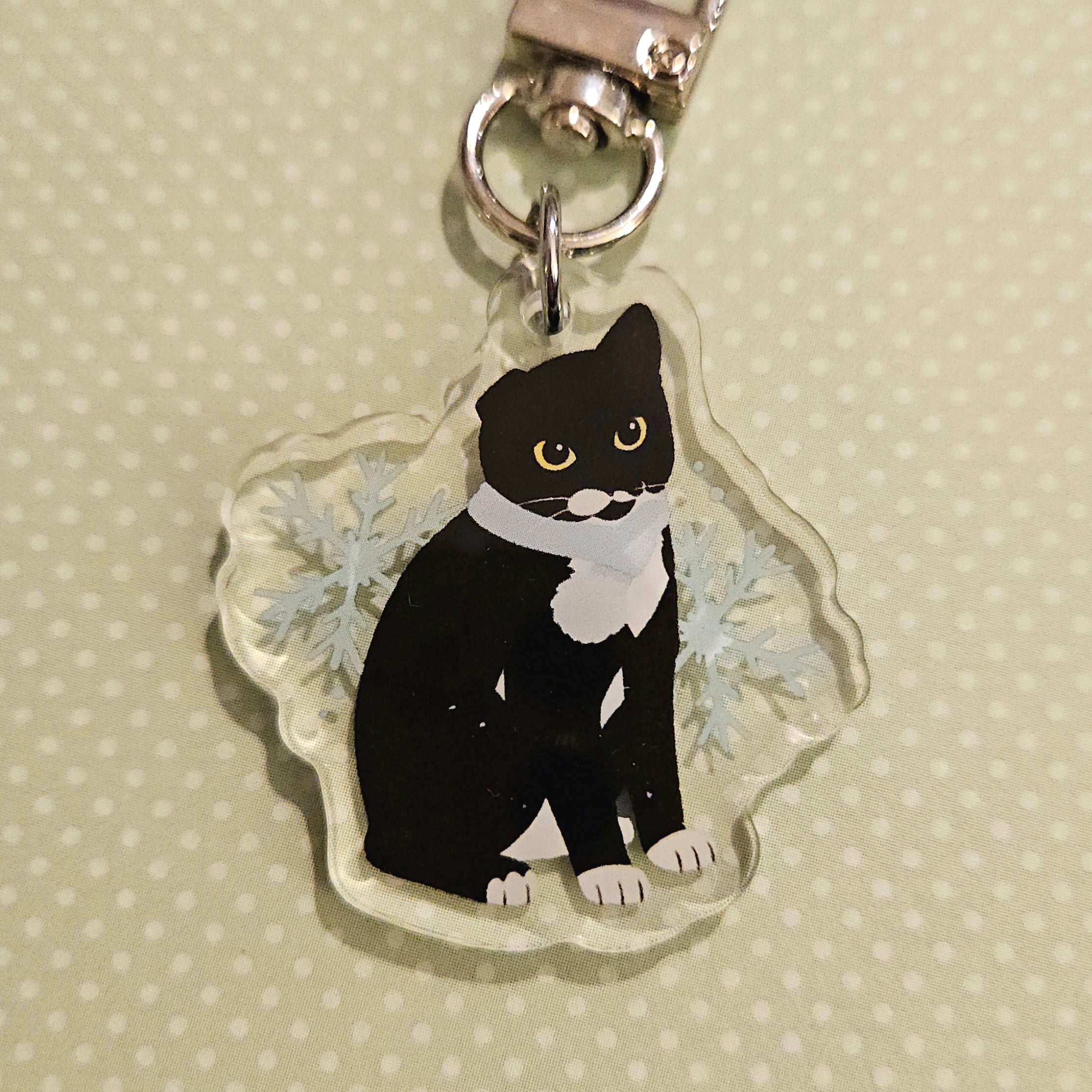 black cat with a scarf and white paws on a snowflake backdrop on a light yellow polkadot background