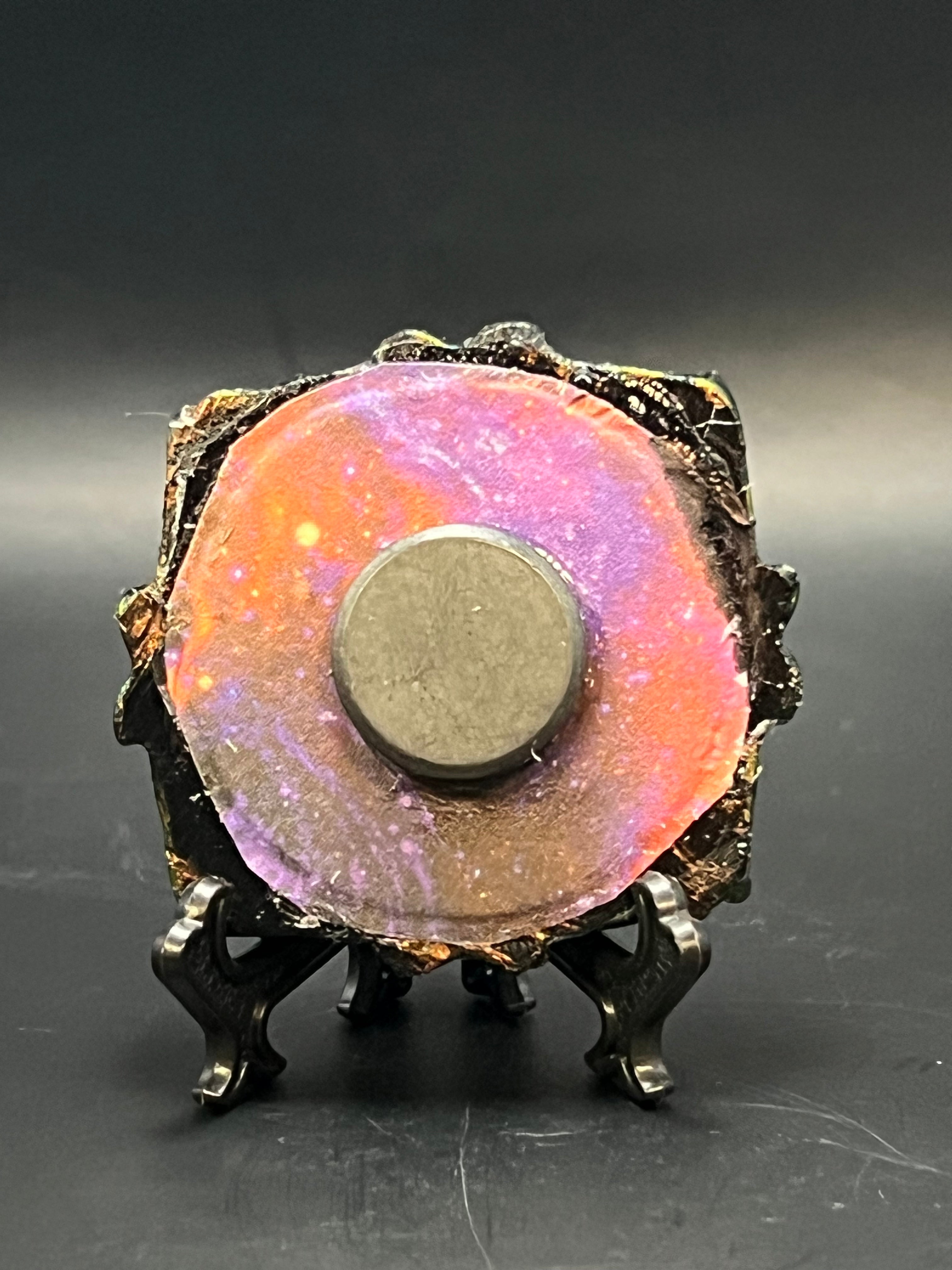 This is the handmade Ascension Miniature Painting by Chris Foster Design. This is showcasing the back.  This is a small heart frame and the decorative item with a sparkly mix background with pink, orange and purple on a stand with yellow stars. There is a magnet and against a miniature picture frame.