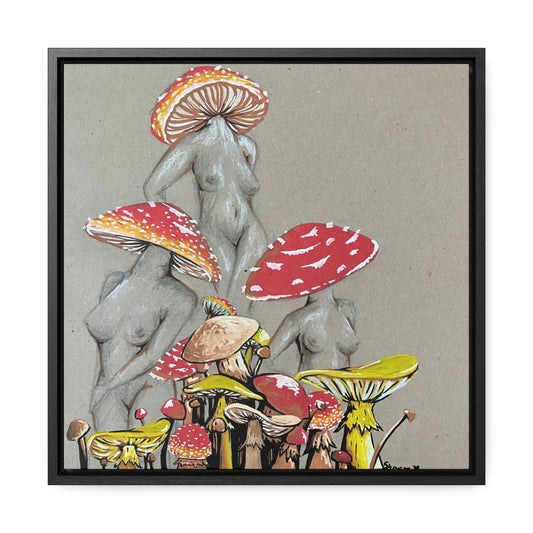 This is the 16" x 16" Miss Amanita Gallery Canvas Wrap with Black Square Frame by Storm Garden Studio. The depth of the frame is 1.25". The image shows the canvas flat on a white wall. This is an illustration of three mushroom headed nude women. The foreground has assorted mushrooms in different sizes. The women are positioned in a triangle shape. The colors range from yellow, orange and red. Each of the bodies are shaded in white, black or grey and match the background of the illustration. 