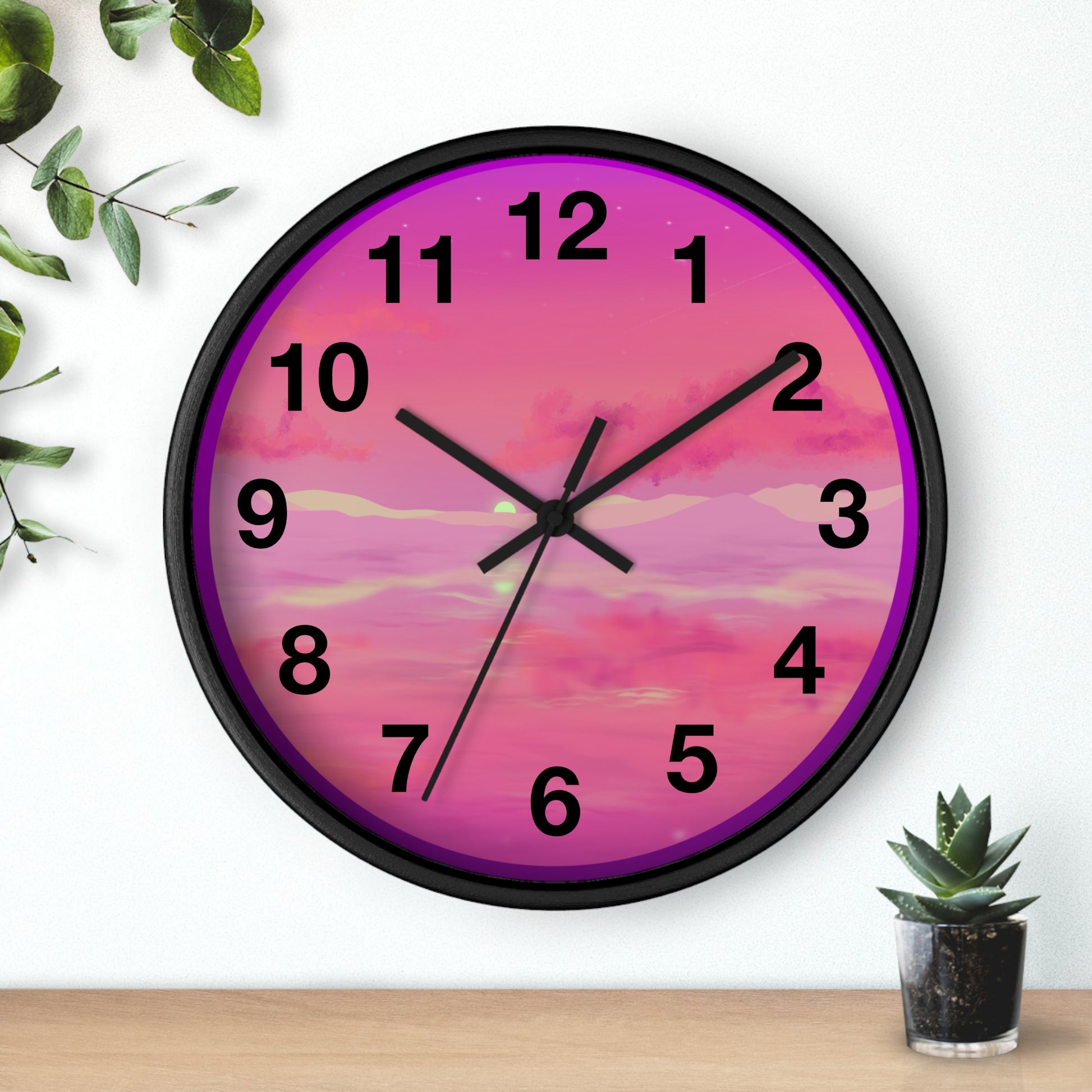 This is the 10" Black Base Pink Dreamscape Wall Clock with black hands by Lee Hansheng Studios.The front of the image with two black clock hands, numerals and the illustration behind it.The illustration has the sky and clouds. Different pinks and hues blended into the clouds and spreads outwards.There are dark purples on the side and yellows near the middle of the art piece. It is on a white background with leaves to the left, succulent plan on the right with a wooden board. 