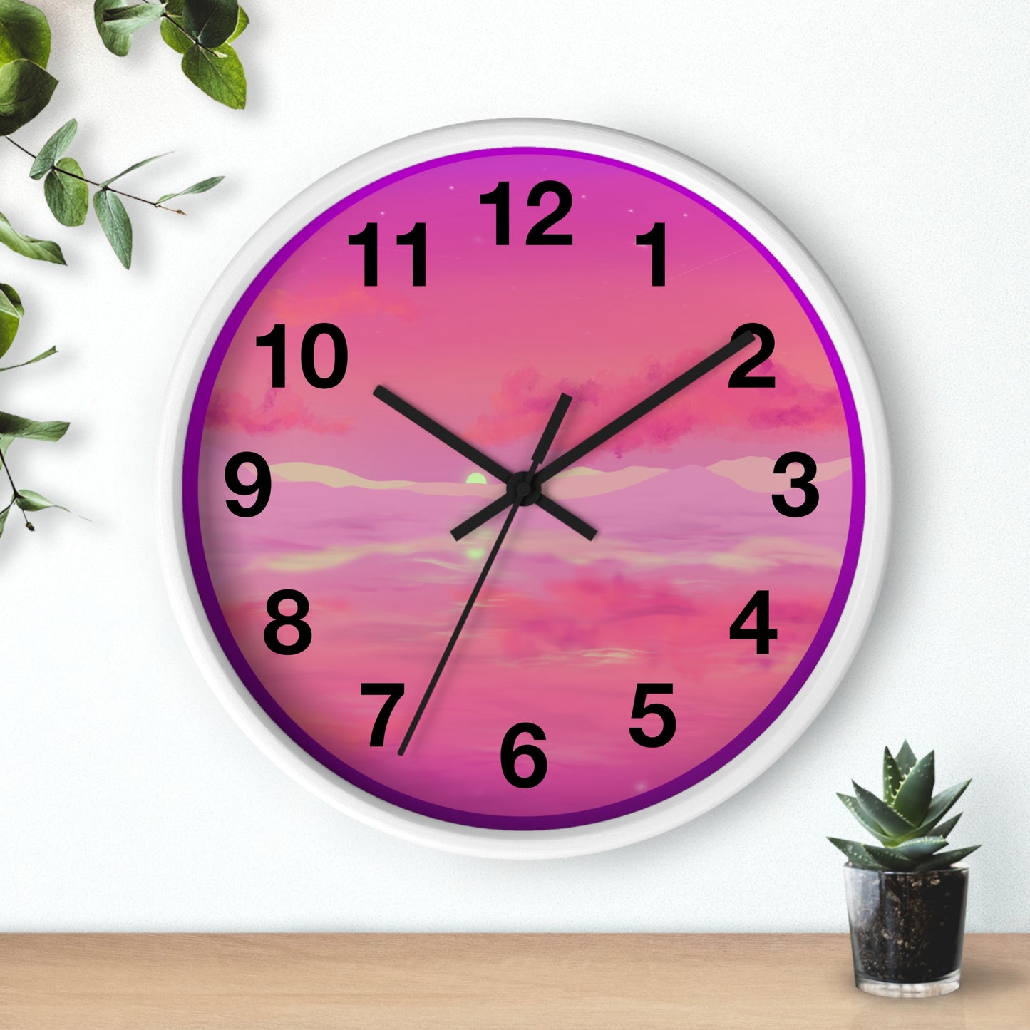 This is the 10" White Base Pink Dreamscape Wall Clock with black hands by Lee Hansheng Studios.The front of the image with two black clock hands, numerals and the illustration behind it.The illustration has the sky and clouds. Different pinks and hues blended into the clouds and spreads outwards.There are dark purples on the side and yellows near the middle of the art piece. It is on a white background with leaves to the left, succulent plan on the right with a wooden board. 