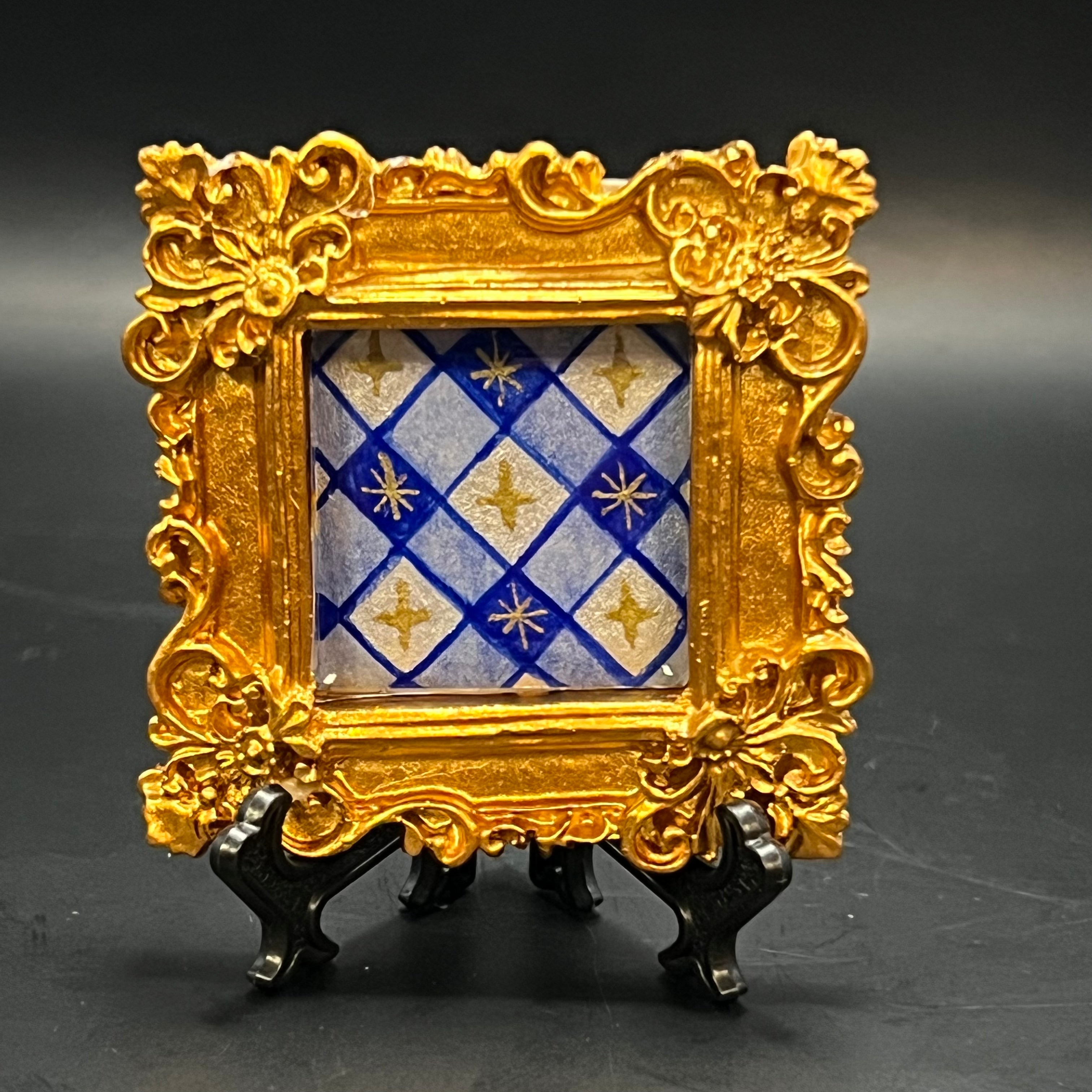 This is the Blue Plaid Stars Mini Painting by Chris Foster Design. This is showcasing the front where a decorative gold frame with a blue and gold patterned plaid, twinkling stars on a black background.