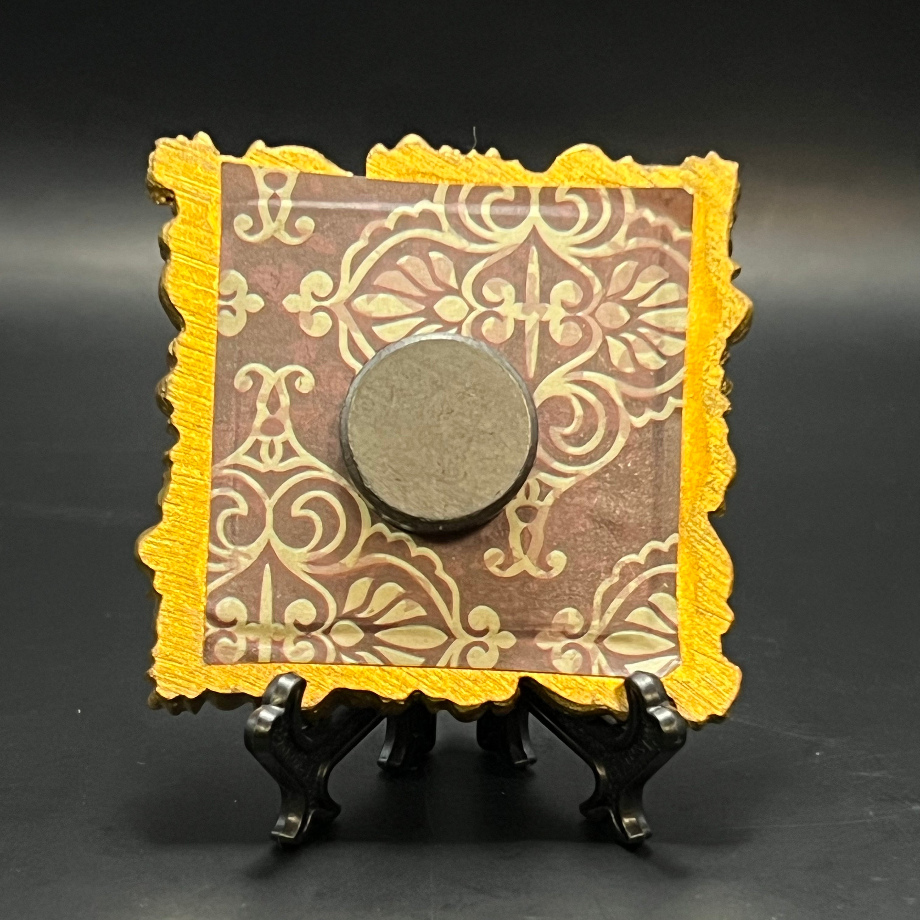 This is the Blue Potion Mini Painting by Chris Foster Design. This is showcasing the back which has a decorative square frame with gold border and intricate patterns, dark brown backing on a black background