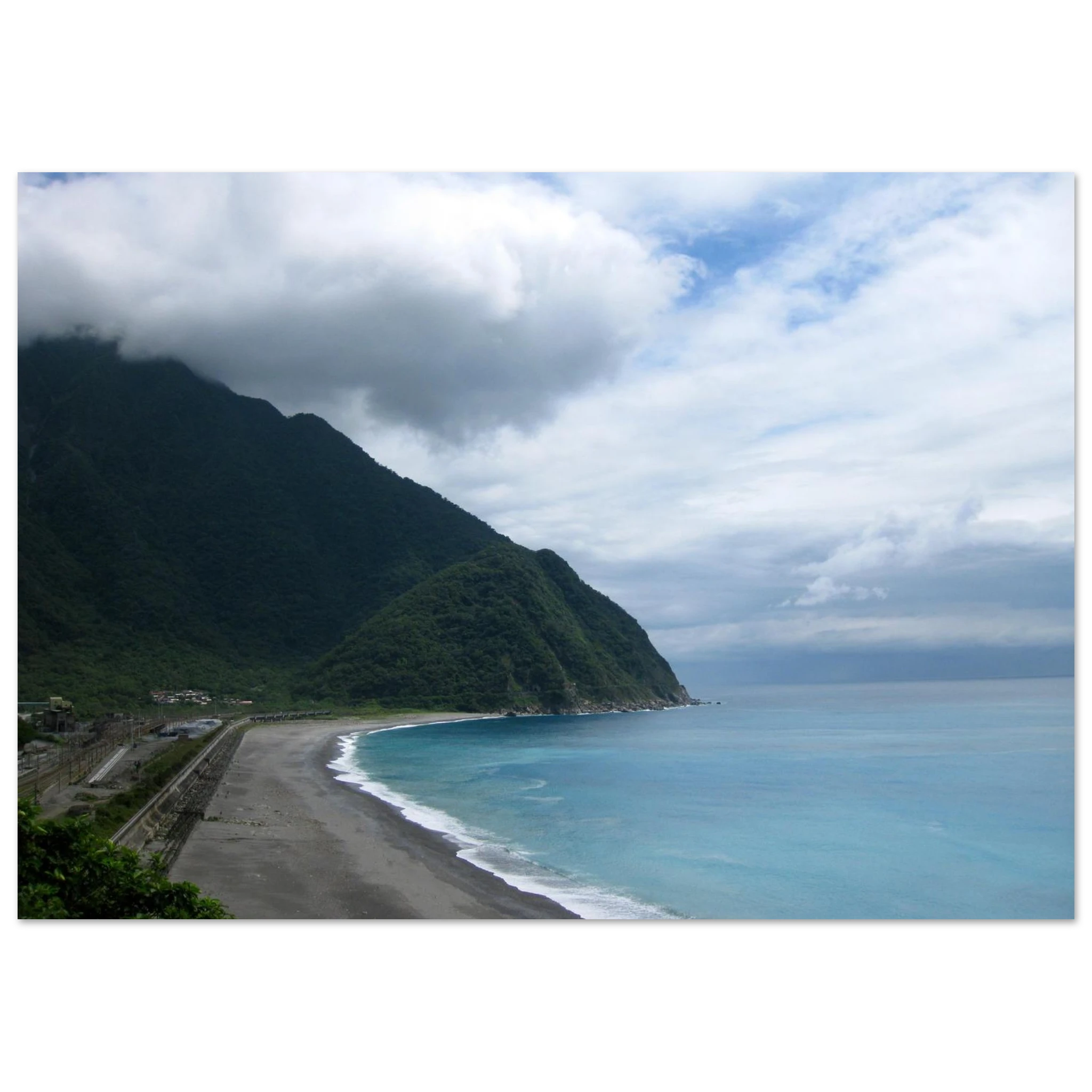 This is the 11" x 14" By Mountains and Sea Print by Lee Hansheng Studios. It is of a famous coast of Taroko National Park in Taiwan. The coastal scene with a beach, dark sand, ocean, and mountains under a cloudy sky. To the left are some houses. Th