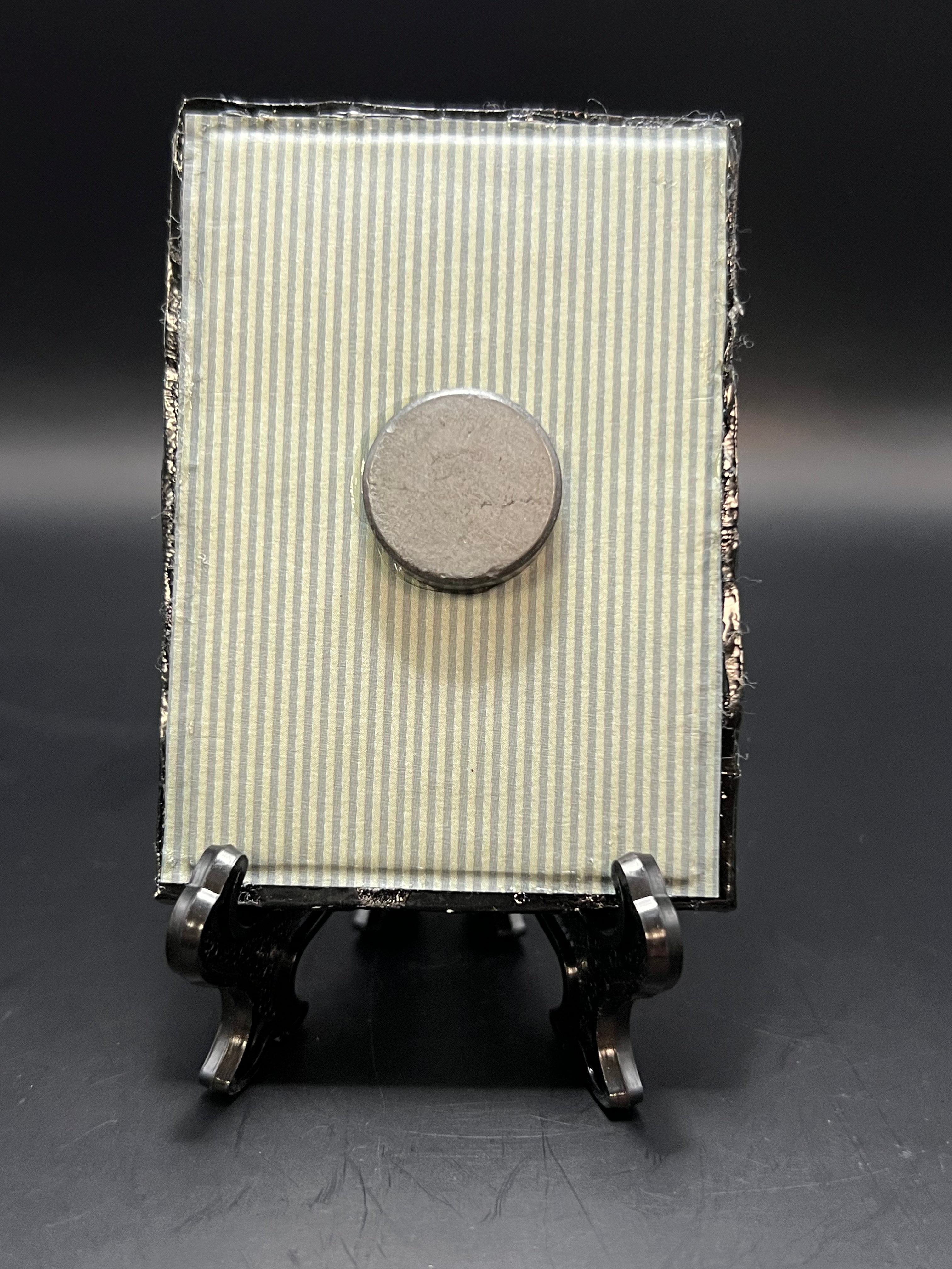 This is the handmade Calosoma Wilcoxi Beetle Miniature Painting by Chris Foster Design. This is showcasing the back. This is a small rectangular frame and the decorative item with a gray and white striped background. There is a magnet and against a miniature picture frame.