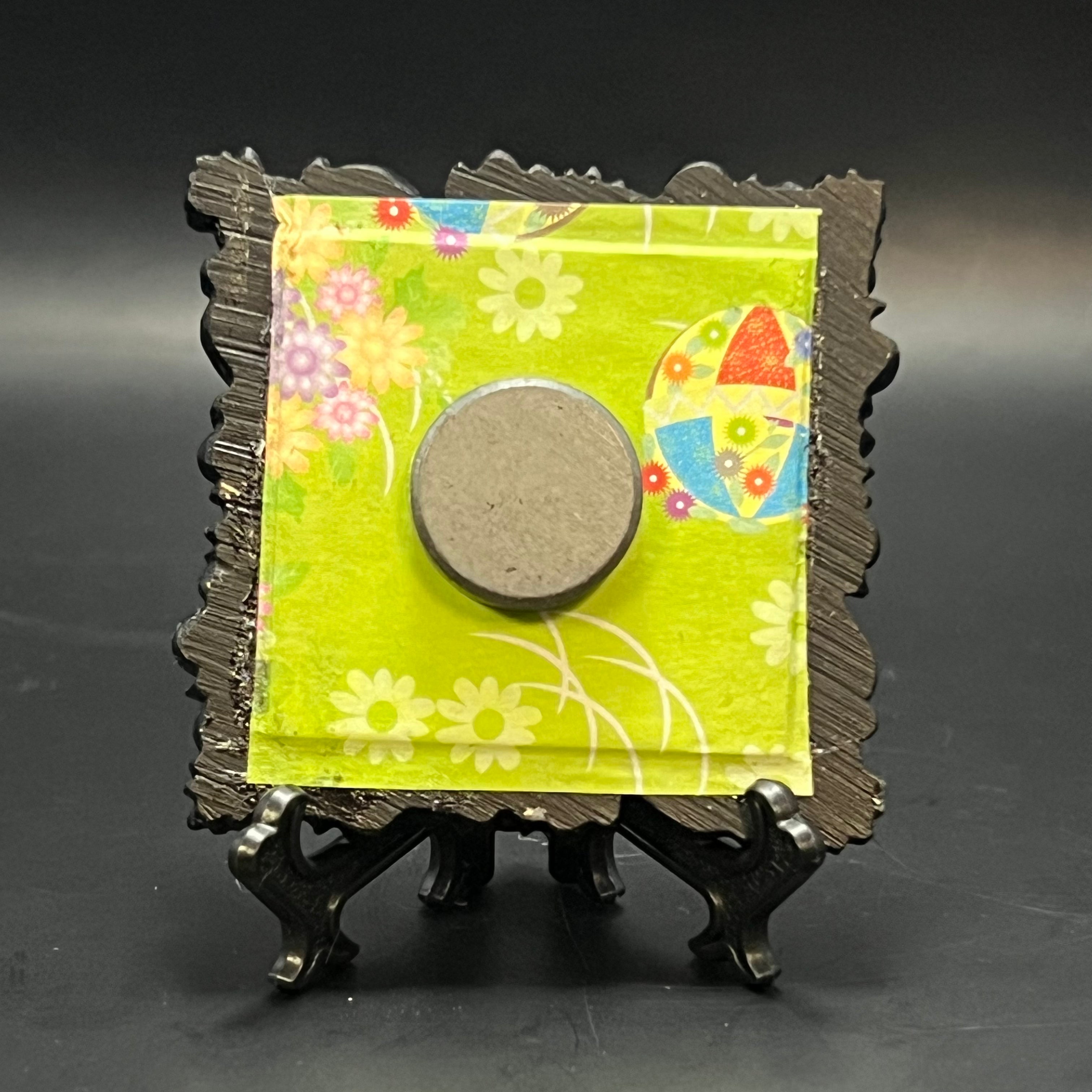 This is the Fly Agaric Mushroom Green Mini Painting by Chris Foster Design. This is showcasing the back. Backed with lime green origami paper with multicolored floral pattern and kamari balls. It is against a dark background.