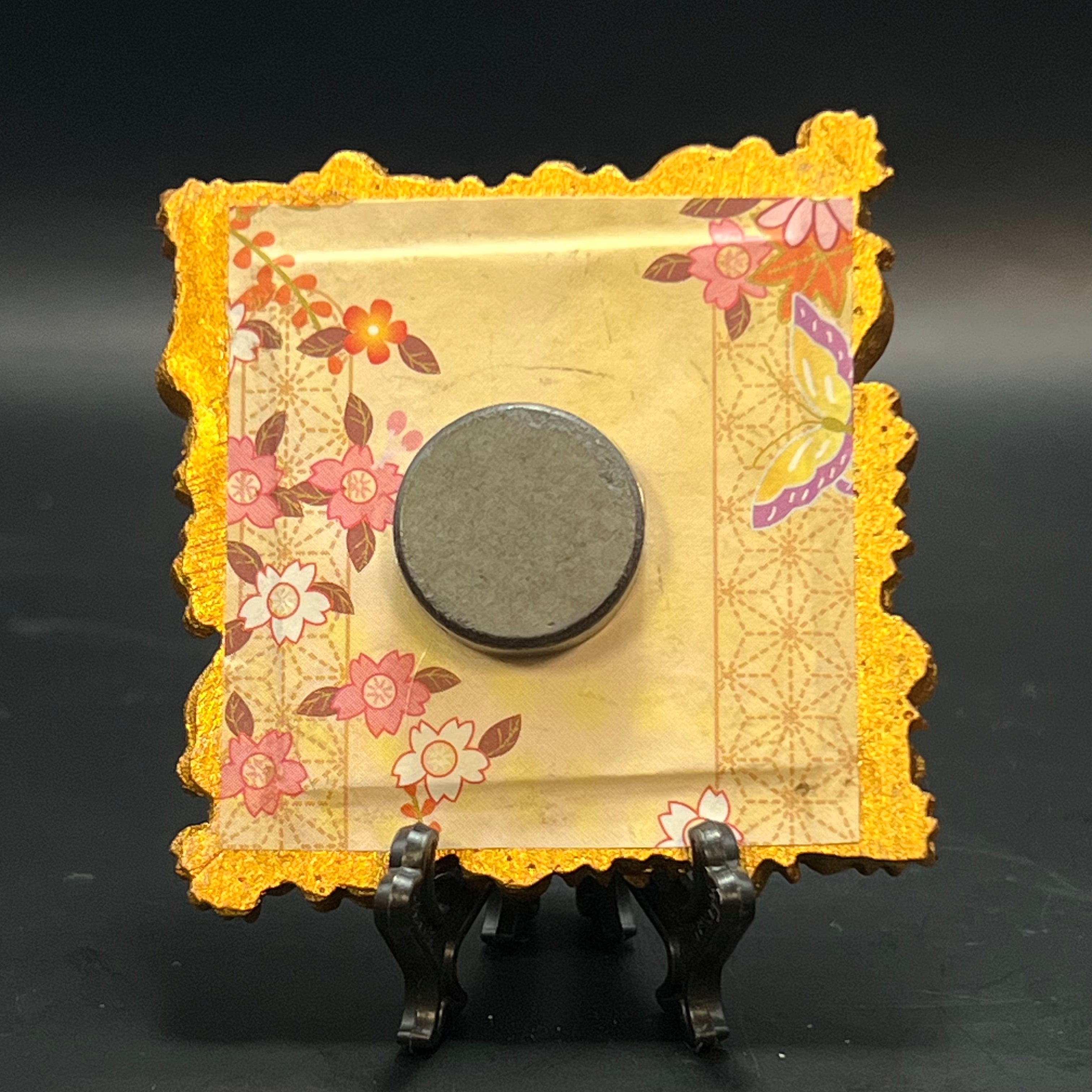 This is the Fly Agaric Orange Mini Painting by Chris Foster Design. This is showcasing the back. Backed with pale yellow, orange, red, brown, and purple floral accent pattern on origami paper. It against a dark background.