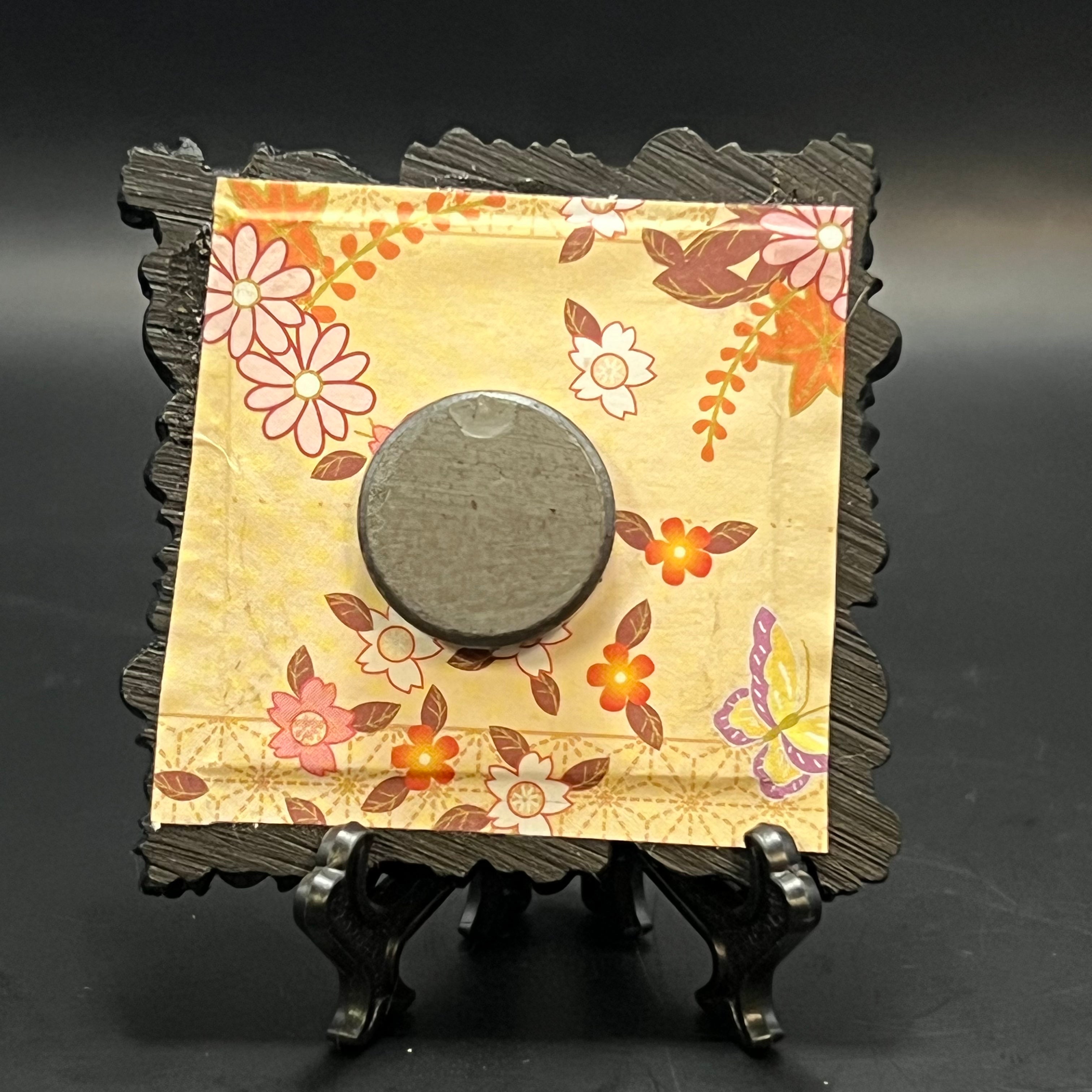 This is the Fly Agaric Yellow Mini Painting by Chris Foster Design. This is showcasing the back. backed with a light yellow, orange, pink, brown, purple, and white butterfly and floral on origami paper. It is against a dark background.