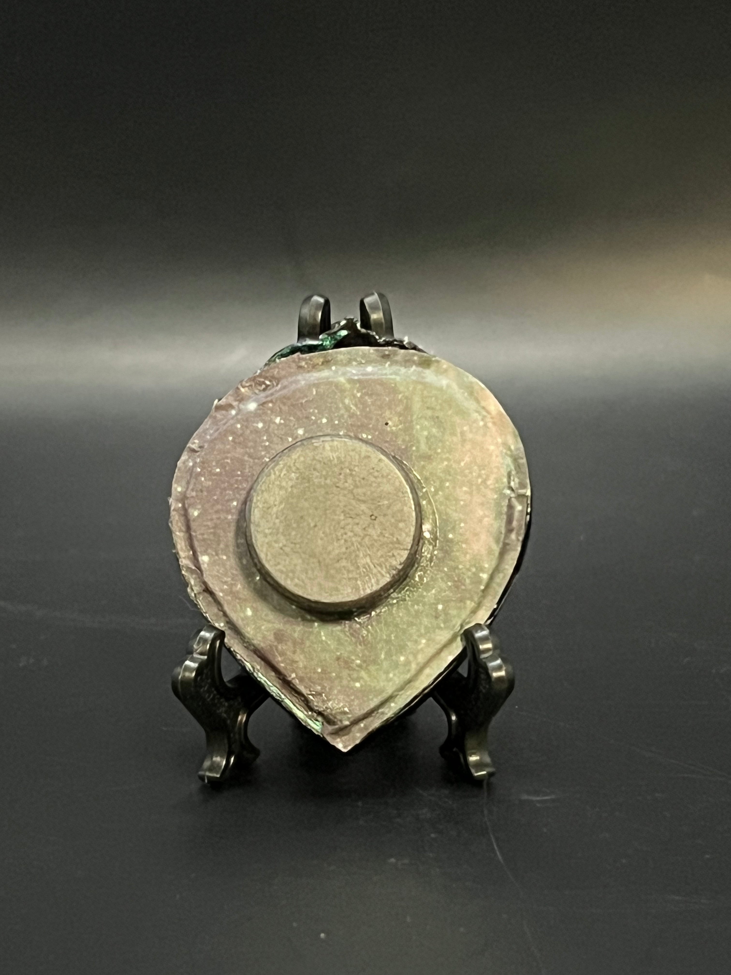 This is the handmade Glowing Cluster Miniature Painting by Chris Foster Design. This is showcasing the back.  This is a small heart frame and the decorative item with a sparkly mix background with green, black and yellow on a stand. There is a magnet and against a miniature picture frame.