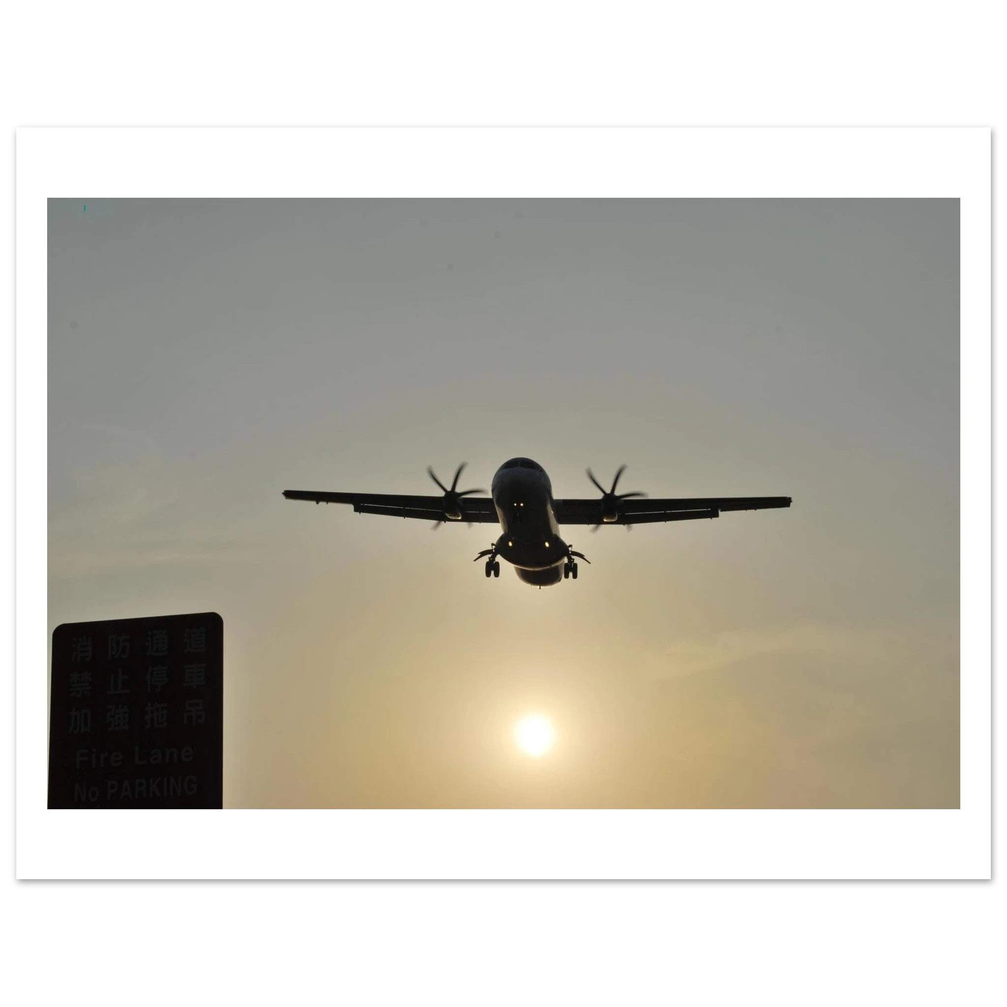This is the 8" x 10" In Bound Print by Lee Hansheng Studios. It was captured at Songshan International Airport in Taipei, Taiwan, when the ATR 72 aircraft is taking flight. The airplane is flying against a sunset sky. On the left corner is a green sign in the shadows. There is a white border around the print. 