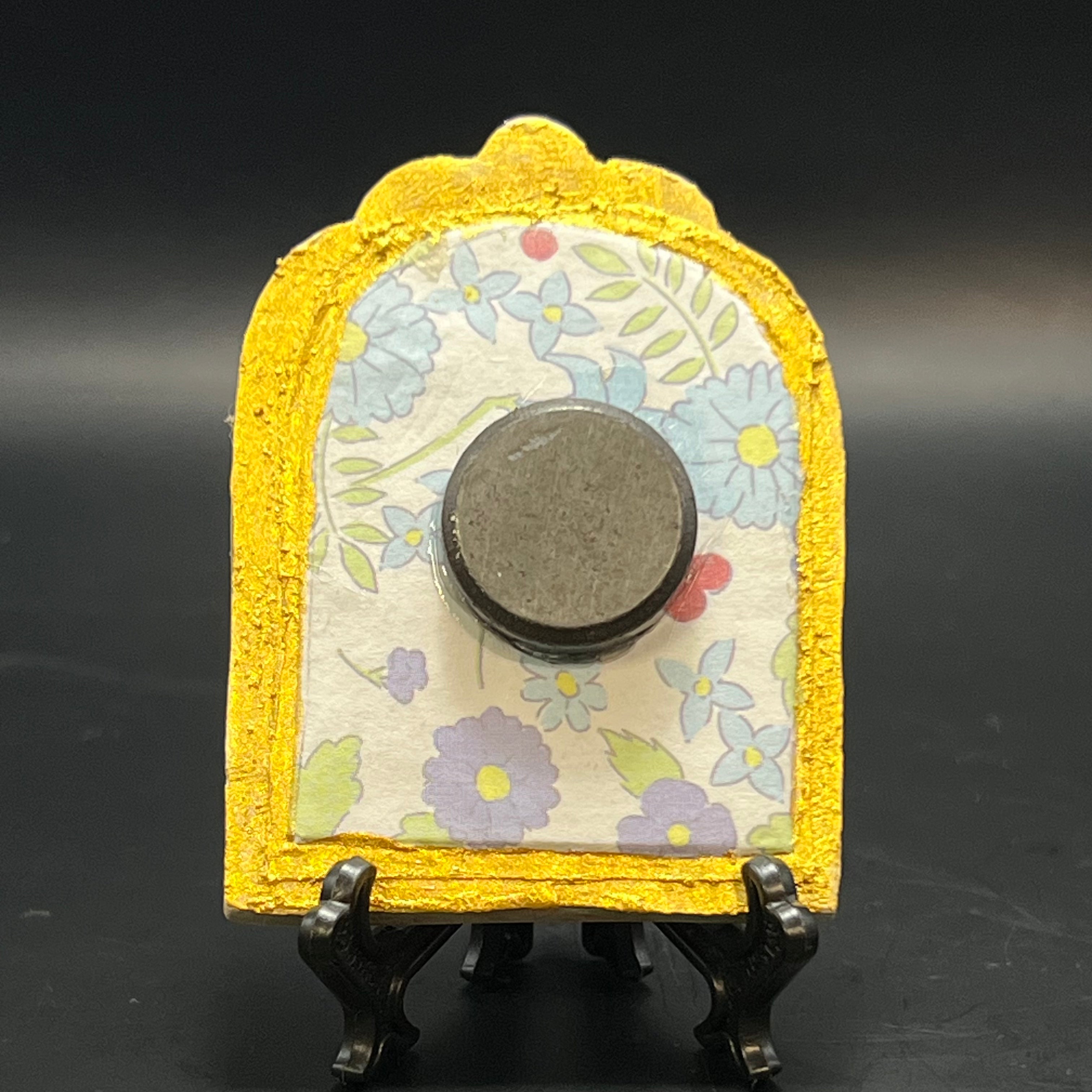 This is the Leucojum Mini Painting by Chris Foster Design. This is showcasing the back. It is backed with a light white, green blue, and purple floral patterned origami paper. It is against a dark background.