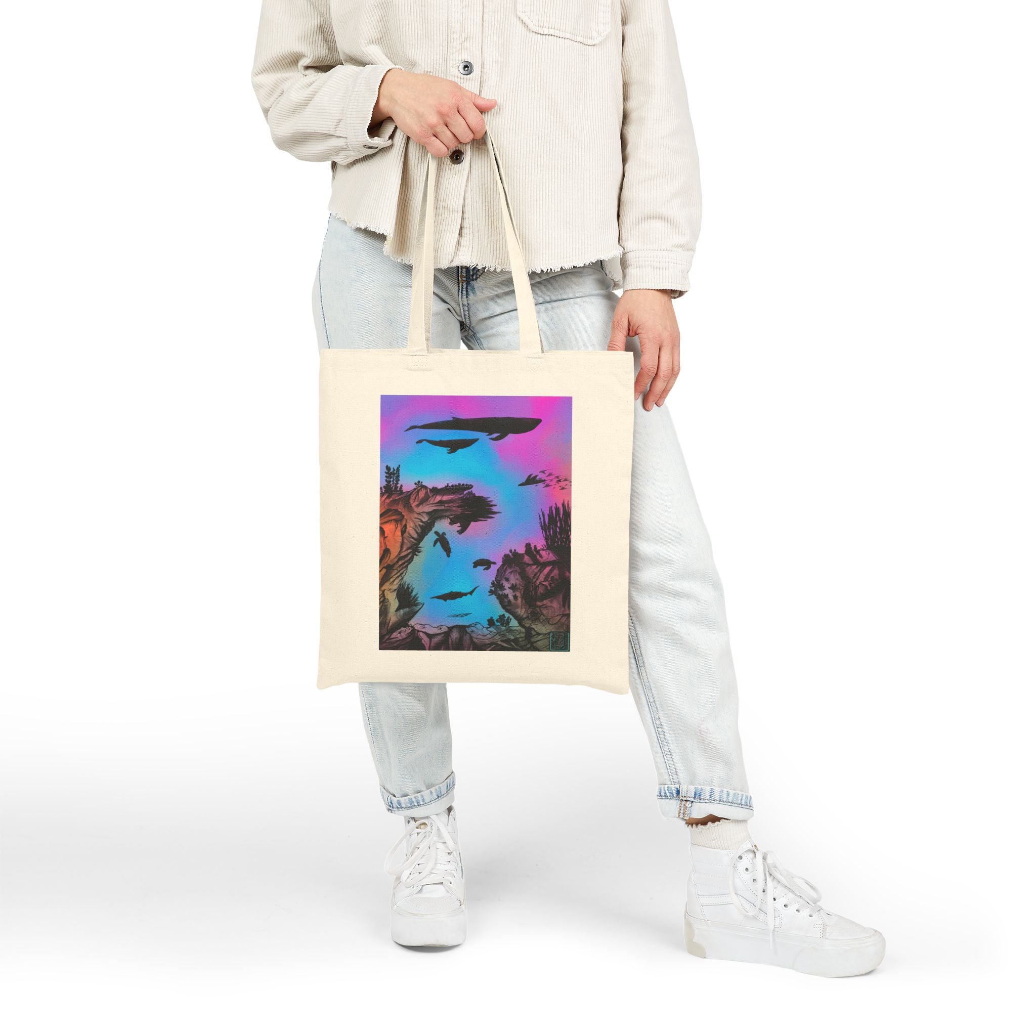 This is Natural Into the Abyss Canvas Tote by Lee Hansheng Studios.The illustration is underwater seascape with aquatic plants on a marbled background.There are two blue whales,1 goblin shark,school of eagle rays,two sea turtles and a school of fish.On the bottom right corner where the front patch of the backpack there is the studio logo printed in black outlined in blue.The colors are pink,purple,blue and red/orange.A person is holding the tote by the handles on the right hand with light colored clothes.