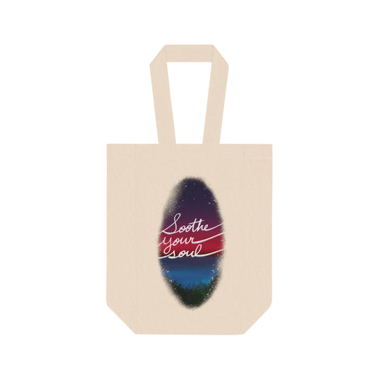 This is the Natural one size Soothe Your Soul Double Wine Tote Bag by Lee Hansheng Studios. This tote securely holds two wine bottles and image showcases the tote from the front. The illustration shows a faded oval drawing of the night sky with white twinkling stars, pink, purple and blue colors. The words shows, "soothe your soul". The tote is against a white background.