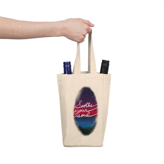 This is the Natural one size Soothe Your Soul Double Wine Tote Bag by Lee Hansheng Studios. This tote securely holds two wine bottles and image showcases the tote from the front. The illustration shows a faded oval drawing of the night sky with white twinkling stars, pink, purple and blue colors. The words shows, "soothe your soul". There is a hand holding the tote from the left with two 25 fl oz (750 ml) wine bottles on each side of the handle. 