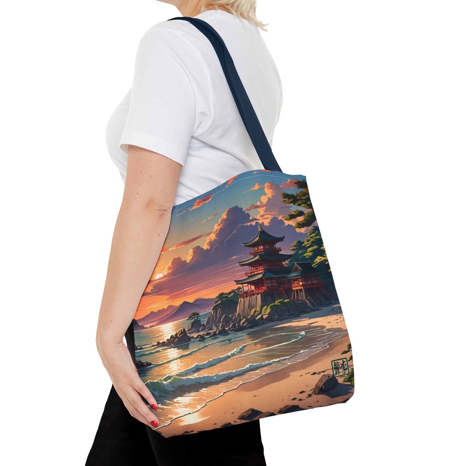 This is the Navy 16" x 16" Temple of Peace All-over Print Tote Bag by Lee Hansheng Studios.The illustration shows a setting red/orange sun above clouds,two blue roof,brown/red walled temples on the right on top of the hills,mountains,blue/white waves into sand and a forest to the right.On the bottom right corner is the logo printed in black for the studio and outlined in blue.A lady carries the tote from the shoulder,a white tee,blond short hair,her hand in the black pants pocket walking towards the left.