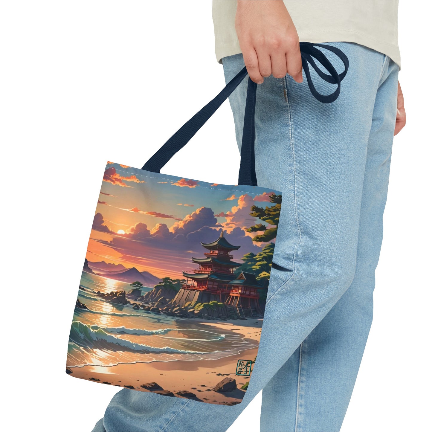 This is the Navy 16" x 16" Temple of Peace All-over Print Tote Bag by Lee Hansheng Studios.The illustration shows a setting red/orange sun above clouds,two blue roof,brown/red walled temples on the right on top of the hills,mountains,blue/white waves into sand and a forest to the right.On the bottom right corner is the logo printed in black for the studio and outlined in blue. The image is of a man wearing white tee, light jeans and right hand is holding the tote from waist down.