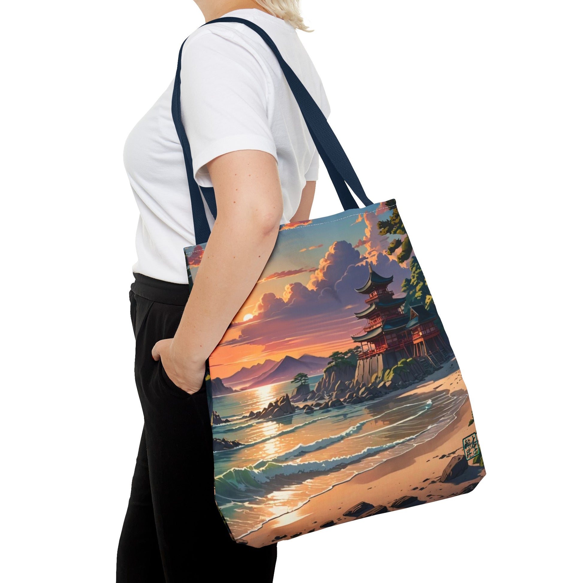 This is the Navy 18" x 18" Temple of Peace All-over Print Tote Bag by Lee Hansheng Studios.The illustration shows a setting red/orange sun above clouds,two blue roof,brown/red walled temples on the right on top of the hills,mountains,blue/white waves into sand and a forest to the right.On the bottom right corner is the logo printed in black for the studio and outlined in blue.A lady carries the tote from the shoulder,a white tee,blond short hair,her hand in the black pants pocket walking towards the left.