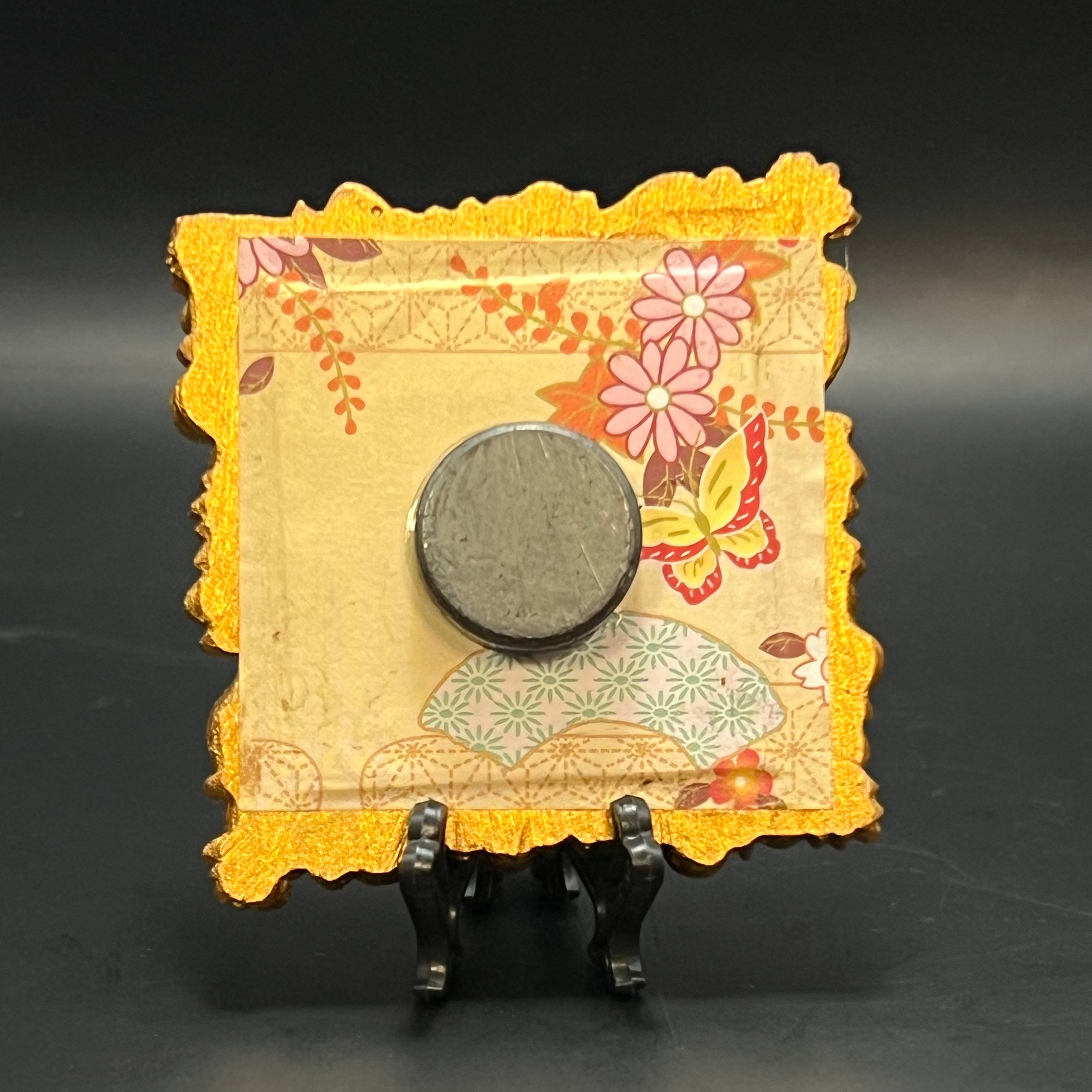 This is the Pumpkin Mini Painting by Chris Foster Design. This is showcasing the back where there's a decorative stand with a floral design with yellow, pink, purple, and red floral butterfly pattern paper holding a round object on a dark background. 