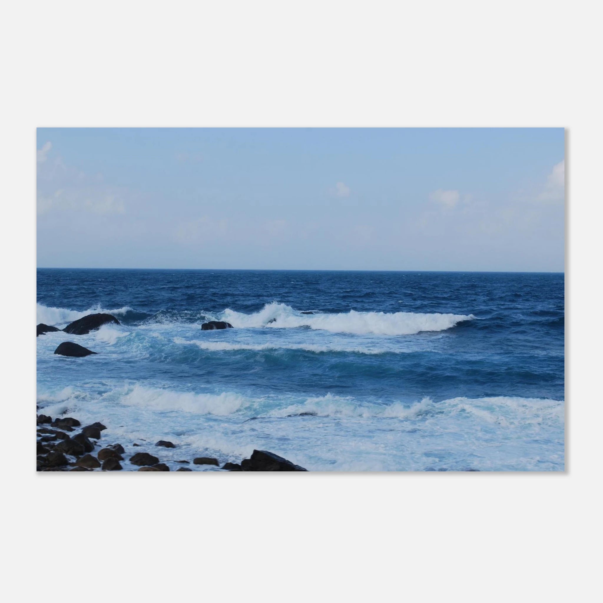 This is the 8" x 12" Rolling Print by Lee Hansheng Studios. This is a photgraph captured from Taiwan's nothern coastline. The waves crash against the rocky shore. The colors range from deep blues and frothy whites as the water comes in. The sky is cloudy with hints of white clouds but the rest is a lighter blue. The print is against a white background. 
