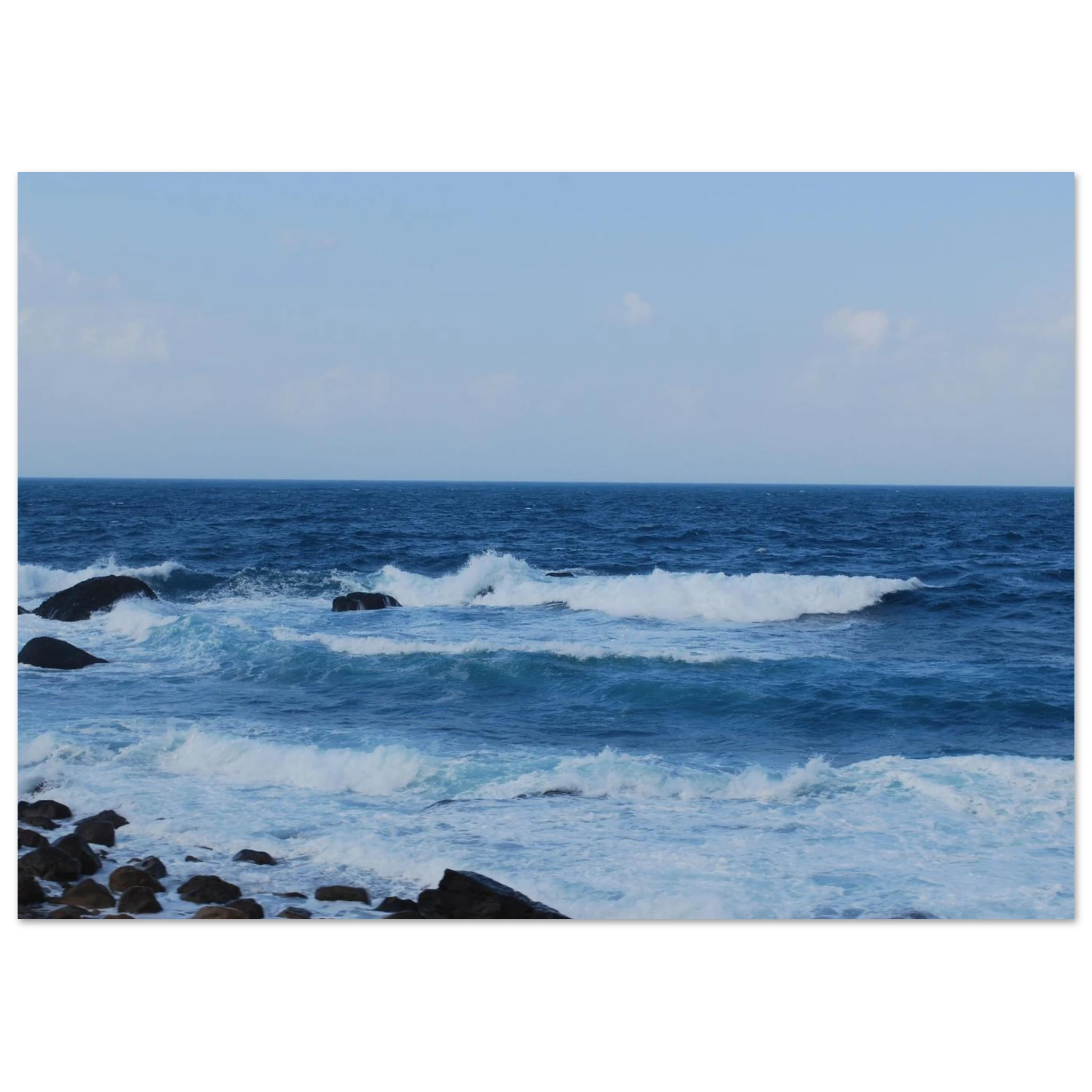 This is the 11" x 14" Rolling Print by Lee Hansheng Studios. This is a photgraph captured from Taiwan's nothern coastline. The waves crash against the rocky shore. The colors range from deep blues and frothy whites as the water comes in. The sky is cloudy with hints of white clouds but the rest is a lighter blue. 