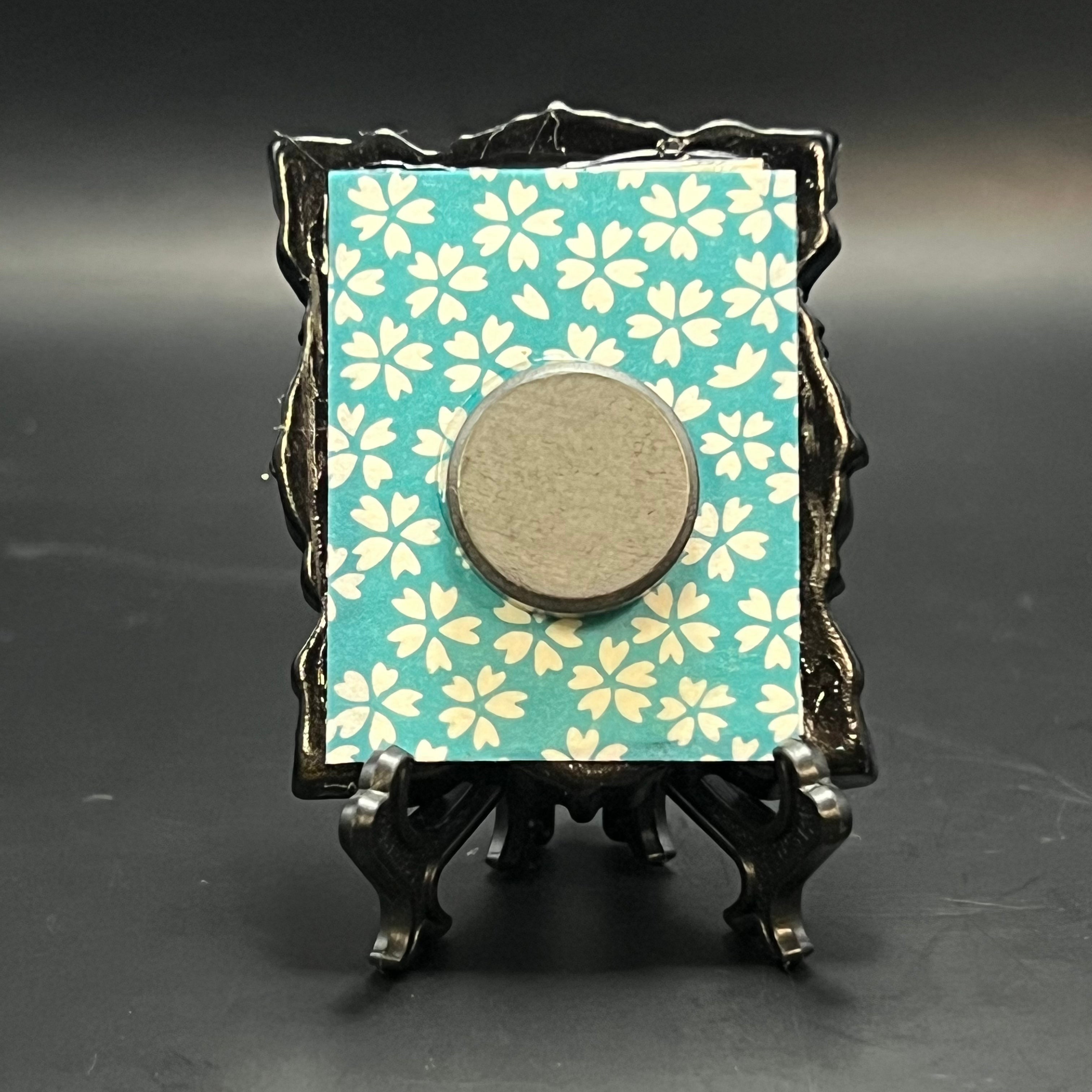 This is the Small Beetle Mini Painting by Chris Foster Design. This is showcasing the back. Backed with bright blue and white cherry blossom pattern origami paper. It is against a dark background.