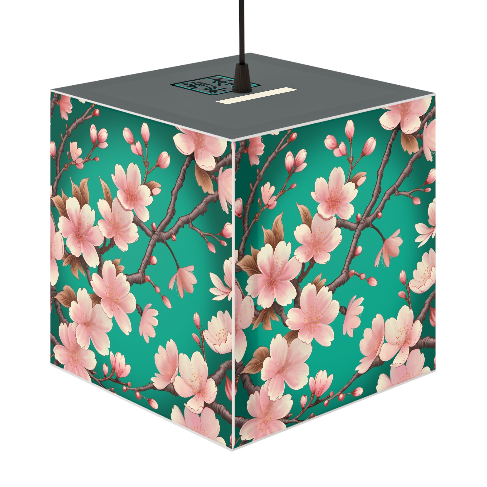 This is the Standard Sakura Light Cube Lamp by Lee Hansheng Studios. The illustration is all around has a blue/teal background, 3-4 thin dark wood branches with pink/light pink buds on each stem. There are blooming and already flowered sakuras on each branch. There is about 3-4 inches between the end of the illustration and the sides of the lamp. It inclused plug for US or EU outlets. The cube lamp is shown hung up. The gray top can be seen with the logo where the cord is being hung.
