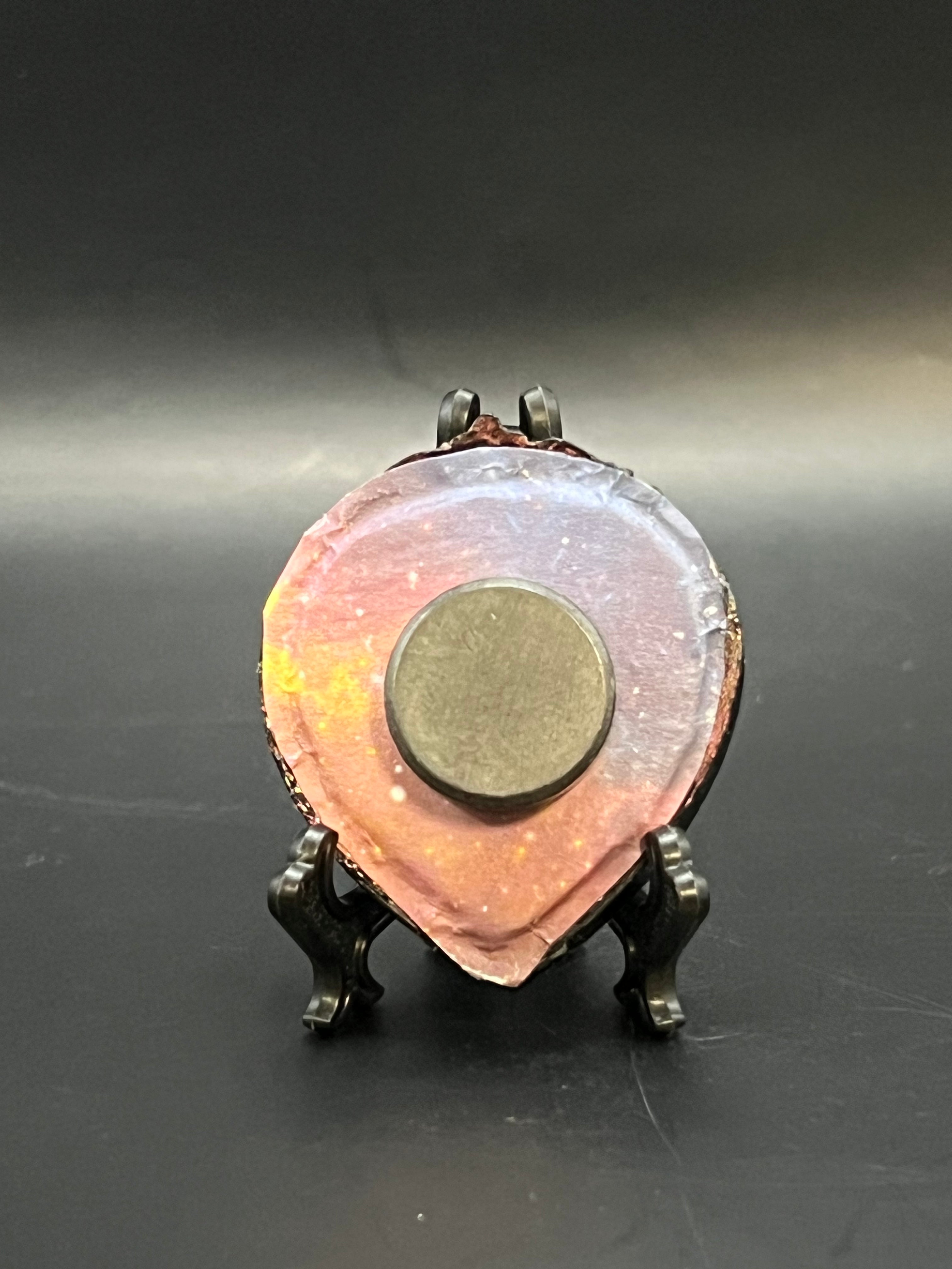 This is the handmade Three Sisters Miniature Painting by Chris Foster Design. This is showcasing the back.  This is a small heart frame and the decorative item with a sparkly mix background with pink, purple, yellow and orange on a stand. There is a magnet and against a miniature picture frame.
