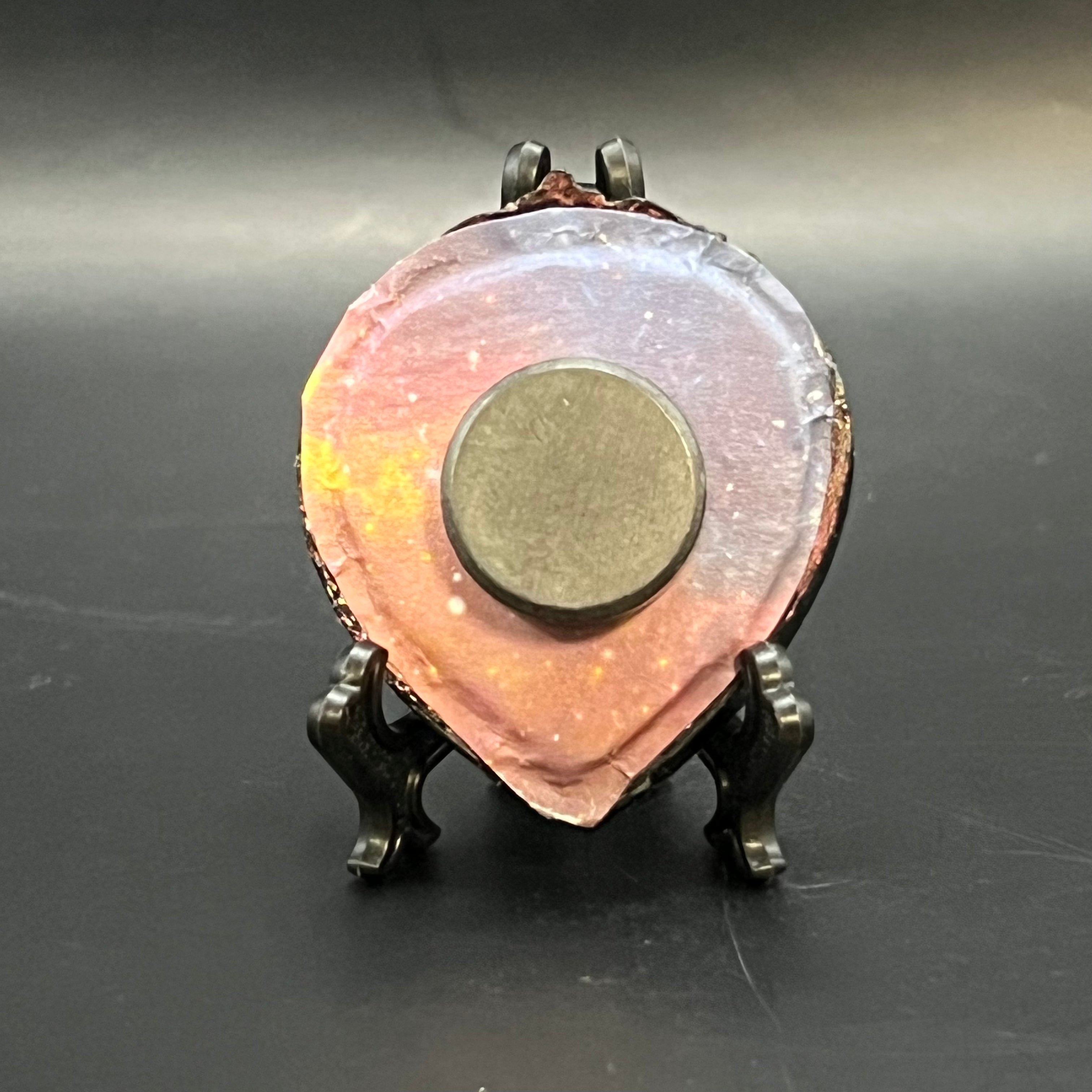 This is the Three Sisters Mini Painting by Chris Foster Design. This is showcasing the back. Backed with a gradient of orange to purple nebula. a round magnet in the middle, on a black stand and against a dark background. 