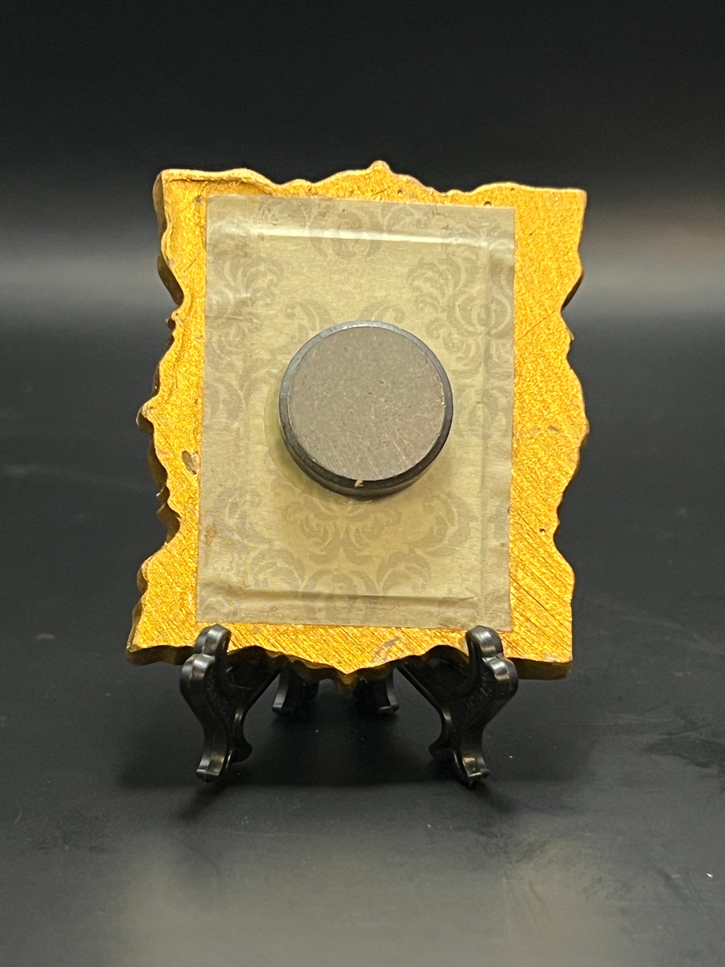 This is the Tulip Mini Painting by Chris Foster Design. This is showcasing the back of it. There is a gold decorative frame with an intricate tan backing. There is a round magnet and it is a black background.