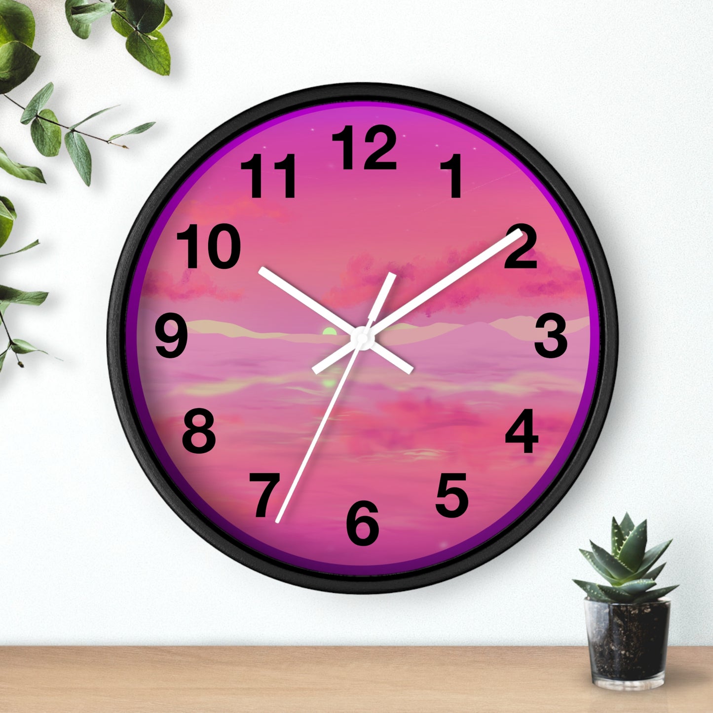 This is the 10" Black Base Pink Dreamscape Wall Clock with white hands by Lee Hansheng Studios.The front of the image with two white clock hands, black numerals and the illustration behind it.The illustration has the sky and clouds. Different pinks and hues blended into the clouds and spreads outwards.There are dark purples on the side and yellows near the middle of the art piece. It is on a white background with leaves to the left, succulent plan on the right with a wooden board. 